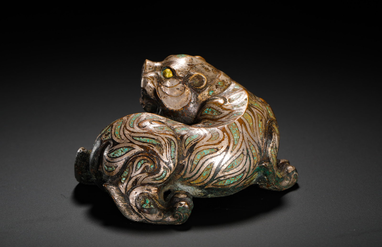 BRONZE WITH SILVER INLAID TURQUOISE RECLINING TIGER FROM THE WARRING STATES PERIOD: Height:7cm (2.76in) Width:11cm (4.33in) Weight:510g(1.12lb)Warring States bronze crouching tiger paperweight inlaid with silver and turquoise, gilded eyes, scroll cloud patterns all over, an ancient d