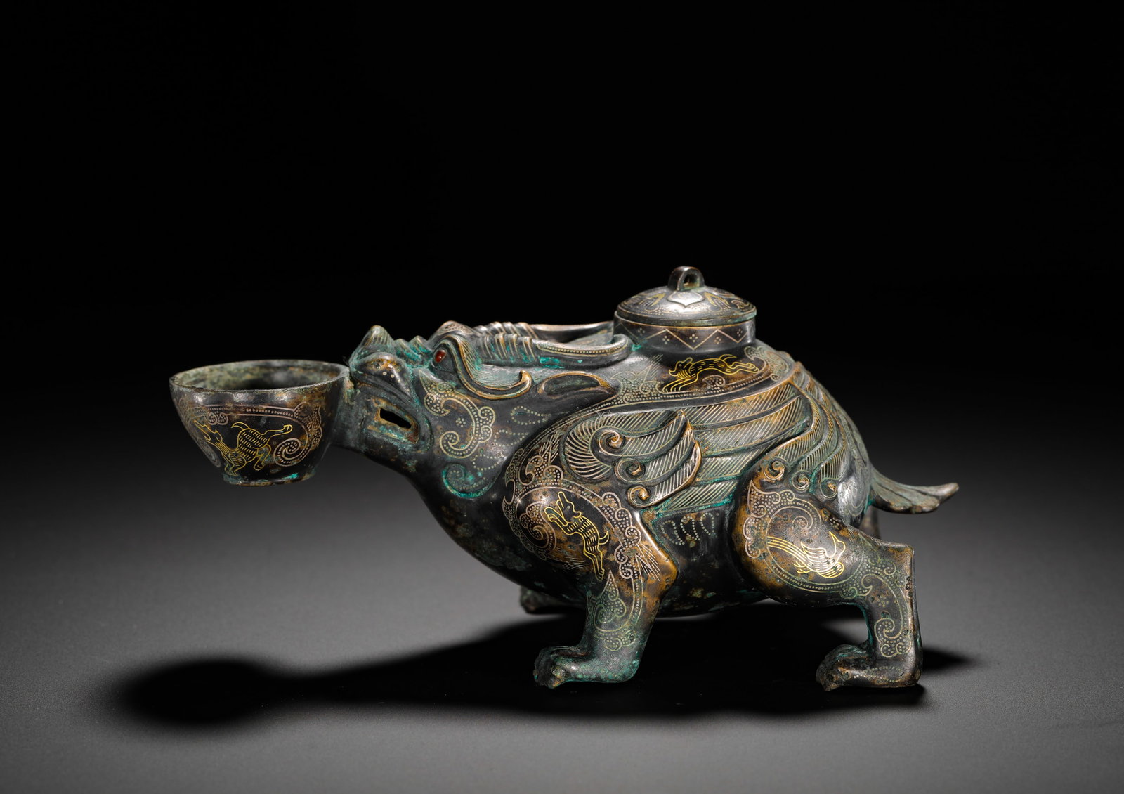 BRONZE OF THE WARRING STATES PERIOD WITH GOLD INLAID AUSPICIOUS BEAST HOLDING A CUP TO DRAW WINE: Height:9cm (3.54in) Width:17cm (6.69in) Weight:600g(1.32lb)Warring States bronze wine vessel with gilded mythical beast holding a cup, interwoven animal engravings and golden inscribed text on base, a