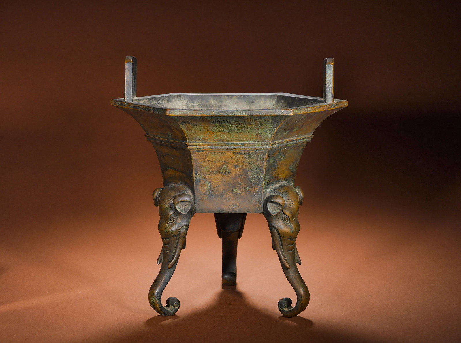 A BRONZE HEXAGONAL ELEPHANT-FOOTED EAR-SHAPED FURNACE FROM THE QING DYNASTY'S QIANLONG PERIOD: Height:37cm Width:35cm Weight:7940gThe whole surface bears naturally aged bronze patina with warm reddish-brown base interspersed with mottled green verdigris permeating the copper body, coated in thi