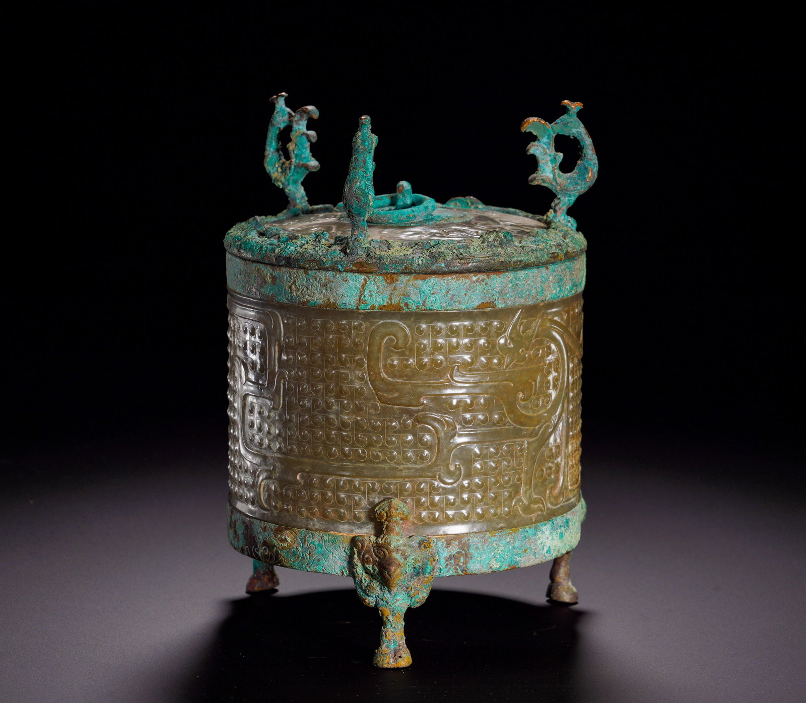 HAN DYNASTY JADE CYLINDER-SHAPED CASKET: Height:15cm (5.91in)Width:12.5cm (4.92in)Weight:1060g(2.34lb)The main body is carved jade decorated with grain patterns and phoenix-dragon motifs. Rim, lid and feet are fitted with bronze fittings. Ph