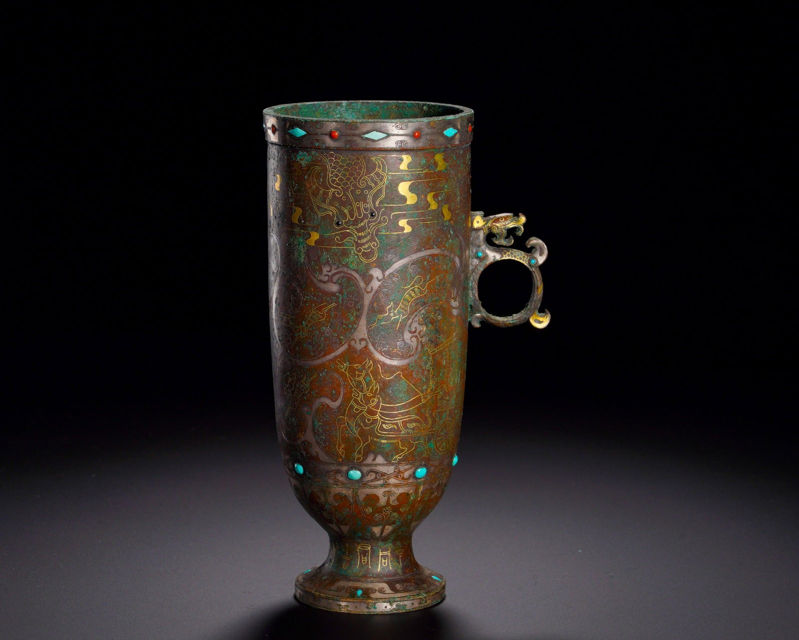 HAN DYNASTY BRONZE INLAID GOLD AND SILVER WITH TURQUOISE EAR CUPS: Height:17.2cm (6.77in)Width:10.5cm (4.13in)Weight:640g(1.41lb)Slender vessel with dragon-head handle inlaid with turquoise. The body is decorated with chariot hunting scenes inlaid with gold and silve