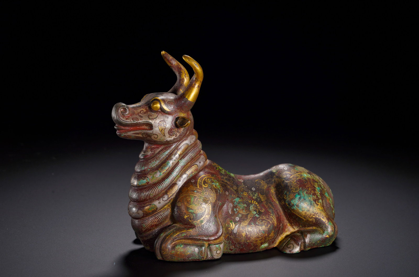 HAN DYNASTY BRONZE INLAID GOLD AND SILVER OX TOWN: Height:12.5cm (4.92in)Width:16cm (6.30in)Weight:750g(1.65lb)The ox lies crouching, head turned sideways, horns decorated with gold inlay. The body is fully ornamented with dragon-phoenix scroll patter
