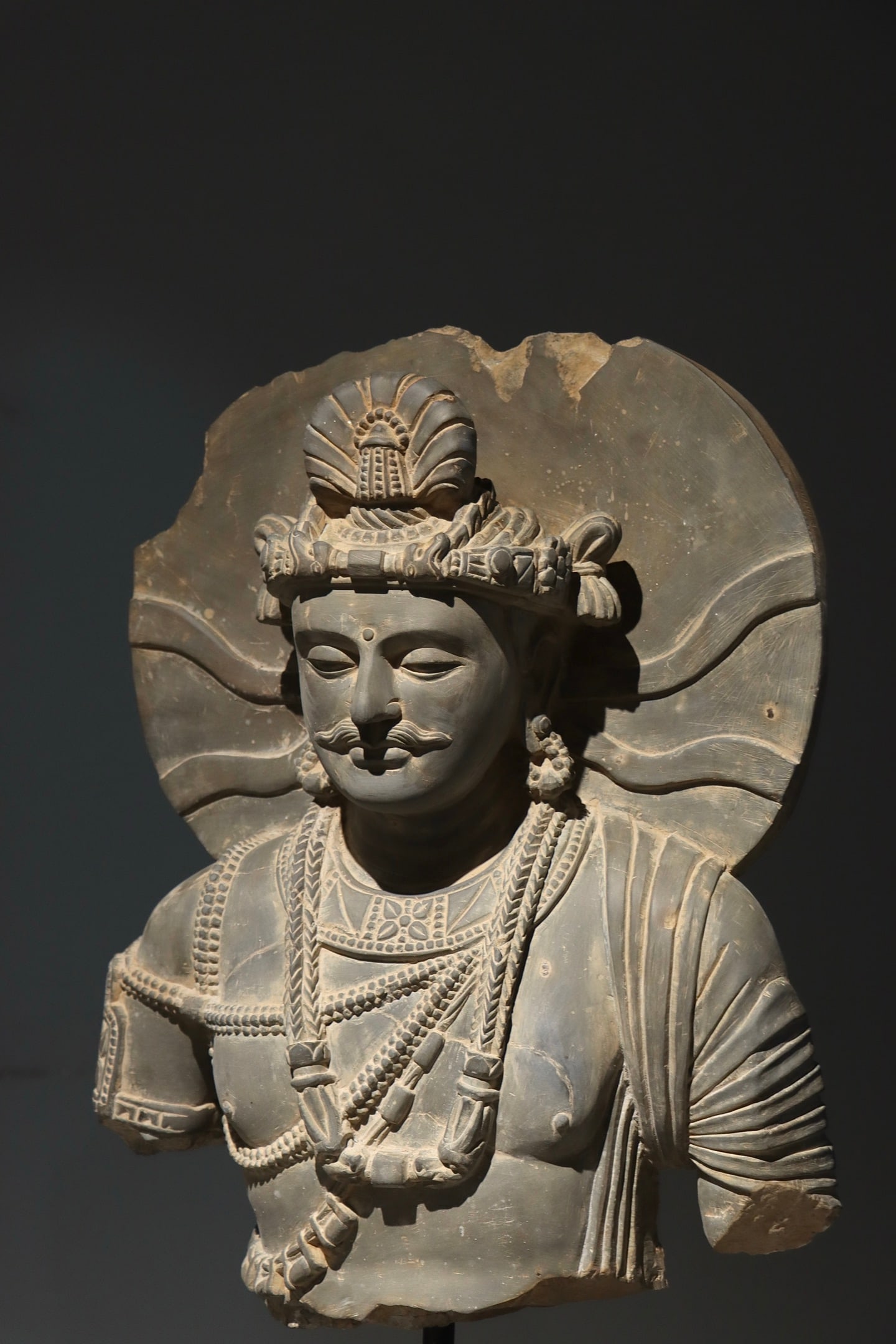 GANDHARA STATUES FROM THE 3RD CENTURY: H:77cm H:55cm This is a fragmentary Gandhara-style stone Bodhisattva sculpture, crowned with an ornate headpiece and halo, adorned with elaborate necklaces, featuring a serene mustached face, embodyin