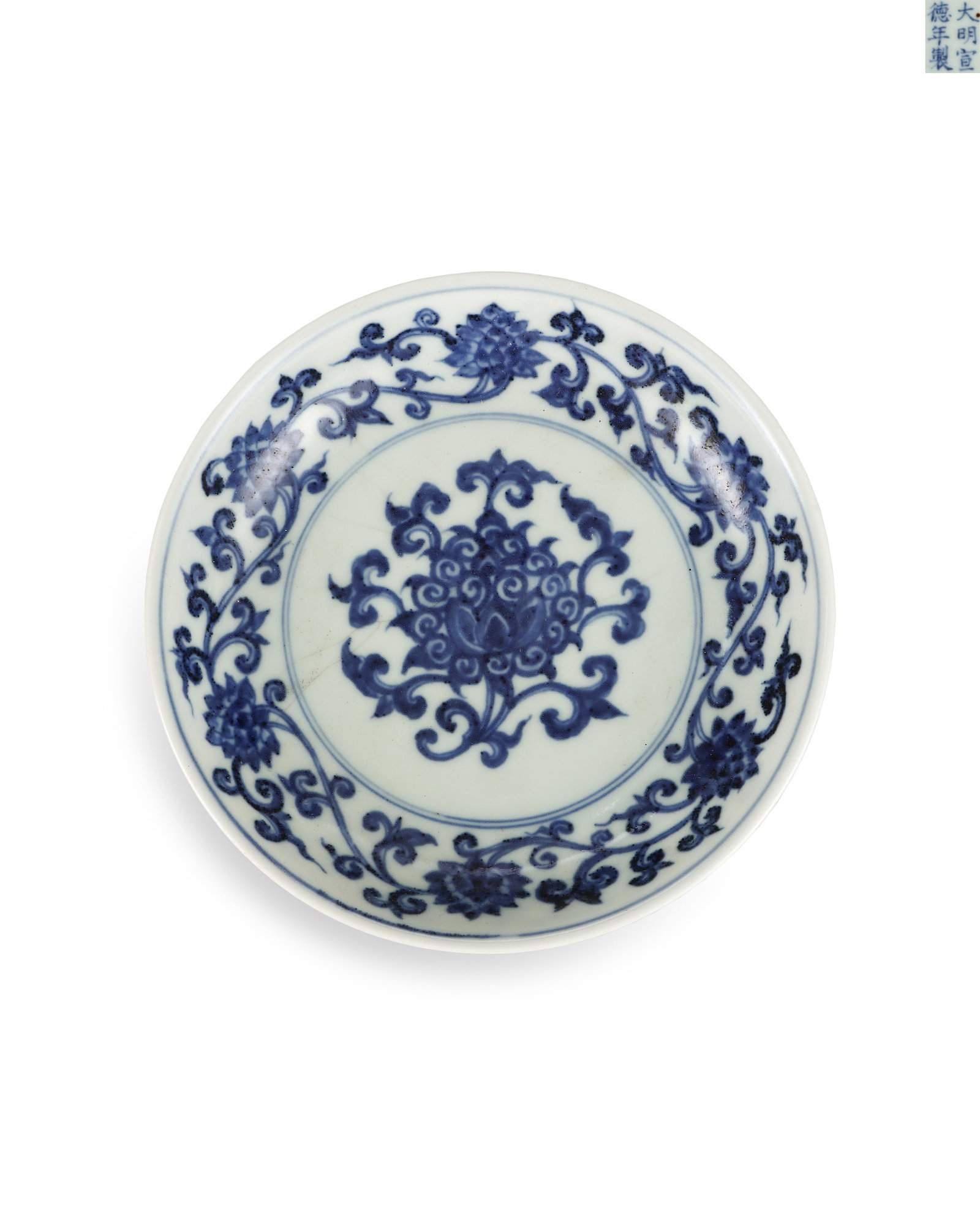 A BLUE AND WHITE PLATE OF THE XUANDE PERIOD OF THE MING DYNASTY: H:3.5cm W:16.8cm This is an imperial blue-and-white plate fired in Xuande reign of Ming Dynasty with glossy white glaze. A single treasure flower is painted at the center, surrounded by a ring of scro