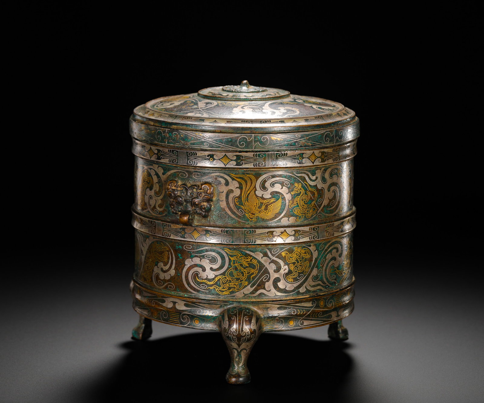 BRONZE INLAID GOLD AND SILVER PHOENIX-PATTERNED CASKET FROM THE WARRING STATES PERIOD: Height:15cm (5.91in) Width:14cm (5.51in) Weight:1700g(3.75lb)Warring States bronze three-legged cosmetic box inlaid with gold and silver phoenix scroll patterns, beast-head ring handle, ancient femini