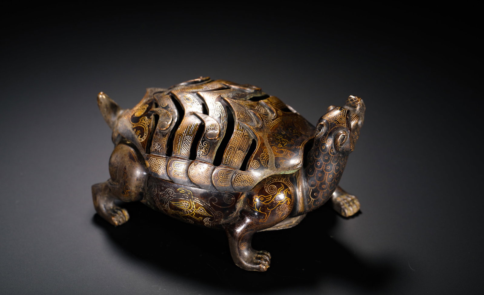 A HAN DYNASTY COPPER INLAID GOLD BASALT TURTLE-SHAPED HOLLOWED-OUT INCENSE BURNER: Height:9cm (3.54in) Width:16.5cm (6.50in) Weight:1030g(2.27lb)Gold-inlaid bronze hollowed-out incense burner shaped as the Xuanwu turtle mythical beast. Aged bronze body with dark brown patina, fully 