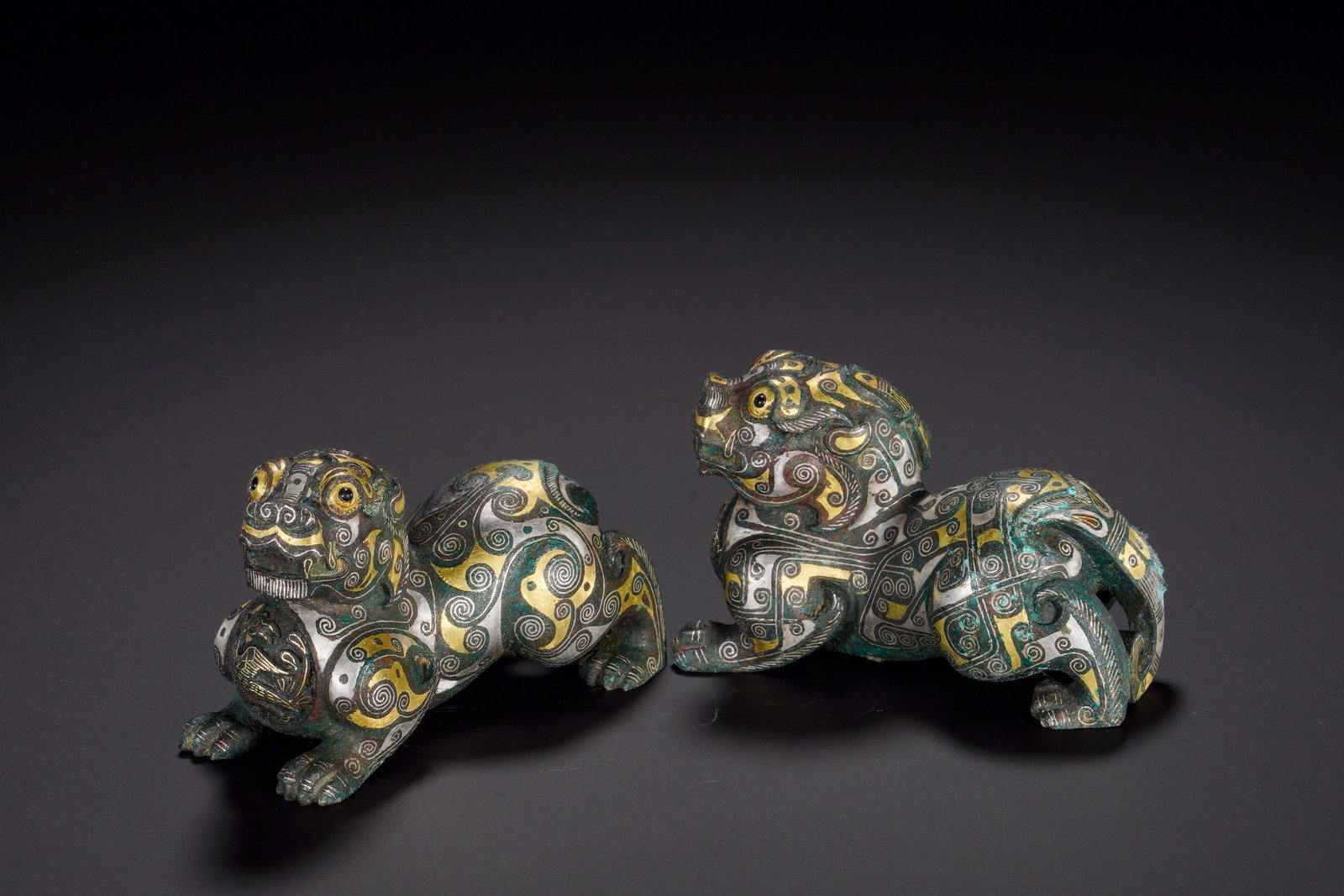 HAN DYNASTY BRONZE INLAID GOLD AND SILVER PAIRS AUSPICIOUS BEAST TOWN: Height:4.5cm (1.77in)Width:8cm (3.15in)Weight:530g(1.17lb)The crouching beasts are decorated with elaborate spiral scroll patterns inlaid with gold and silver, eyes inlaid with stone. Used to secure m