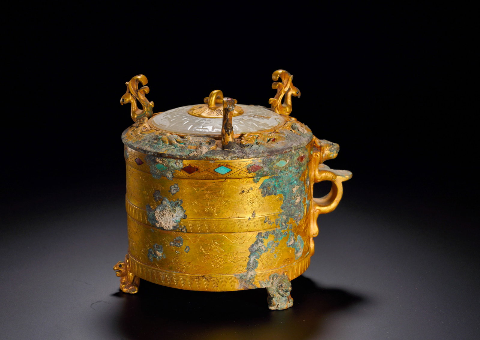 A GILDED COPPER CASKET WITH JADE INLAID IN A CYLINDER FROM THE HAN DYNASTY: Height:16cm (6.30in) Width:13cm (5.12in) Weight:1300g(2.87lb)The gilded bronze container stands on three beast feet, embossed with chariot and beast relief patterns, rim inlaid with turquoise and agat