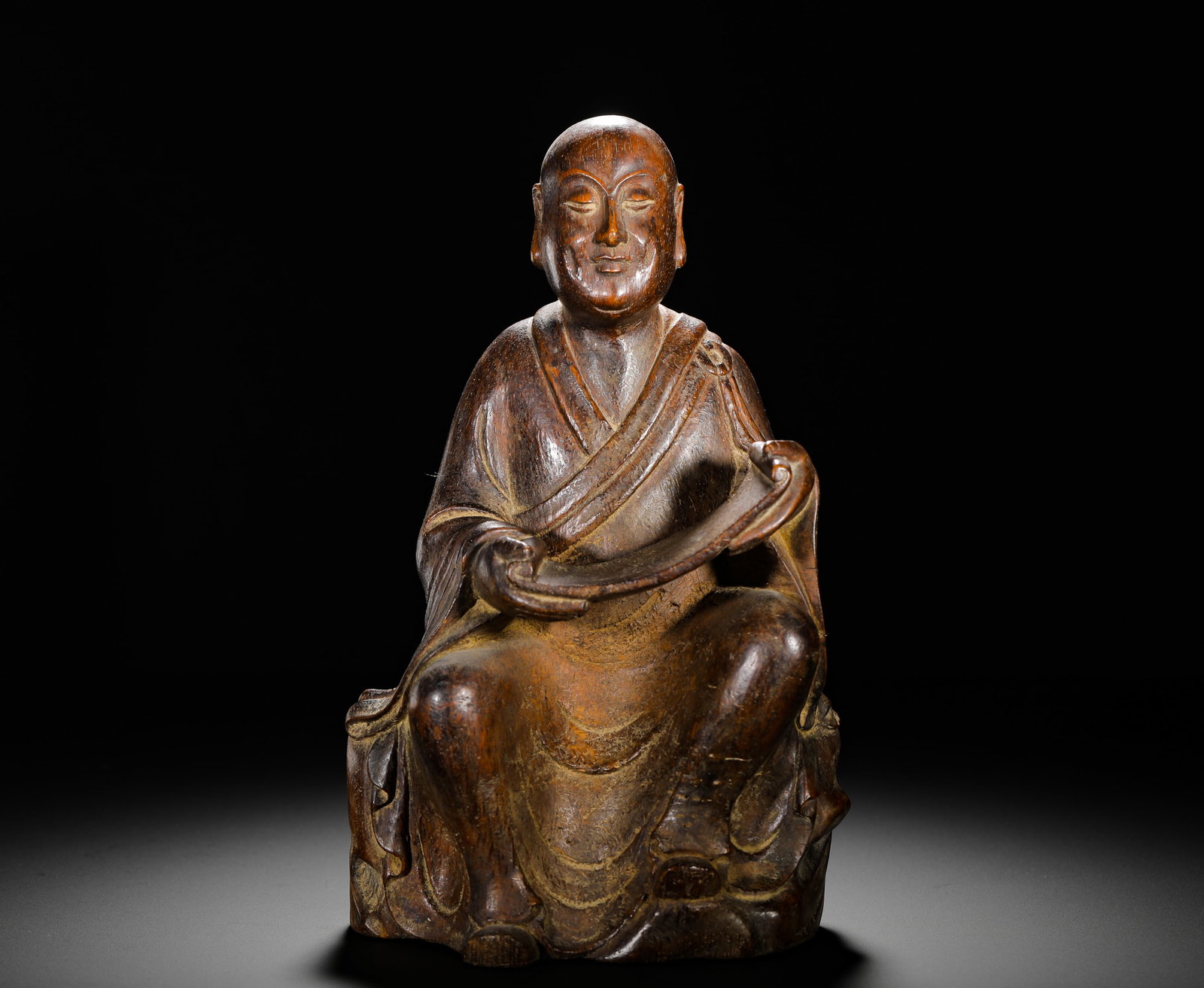 QING DYNASTY BAMBOO-CARVED SEATED FIGURES OF ARHATS HOLDING SCROLLS: Height:25cm (9.84in) Width:15cm (5.91in) Weight:580g(1.28lb)Carved bamboo seated arhat holding scroll, shaved monk head, cross-collar robe, cross-legged on rock base, antique desk carving symbolizing 