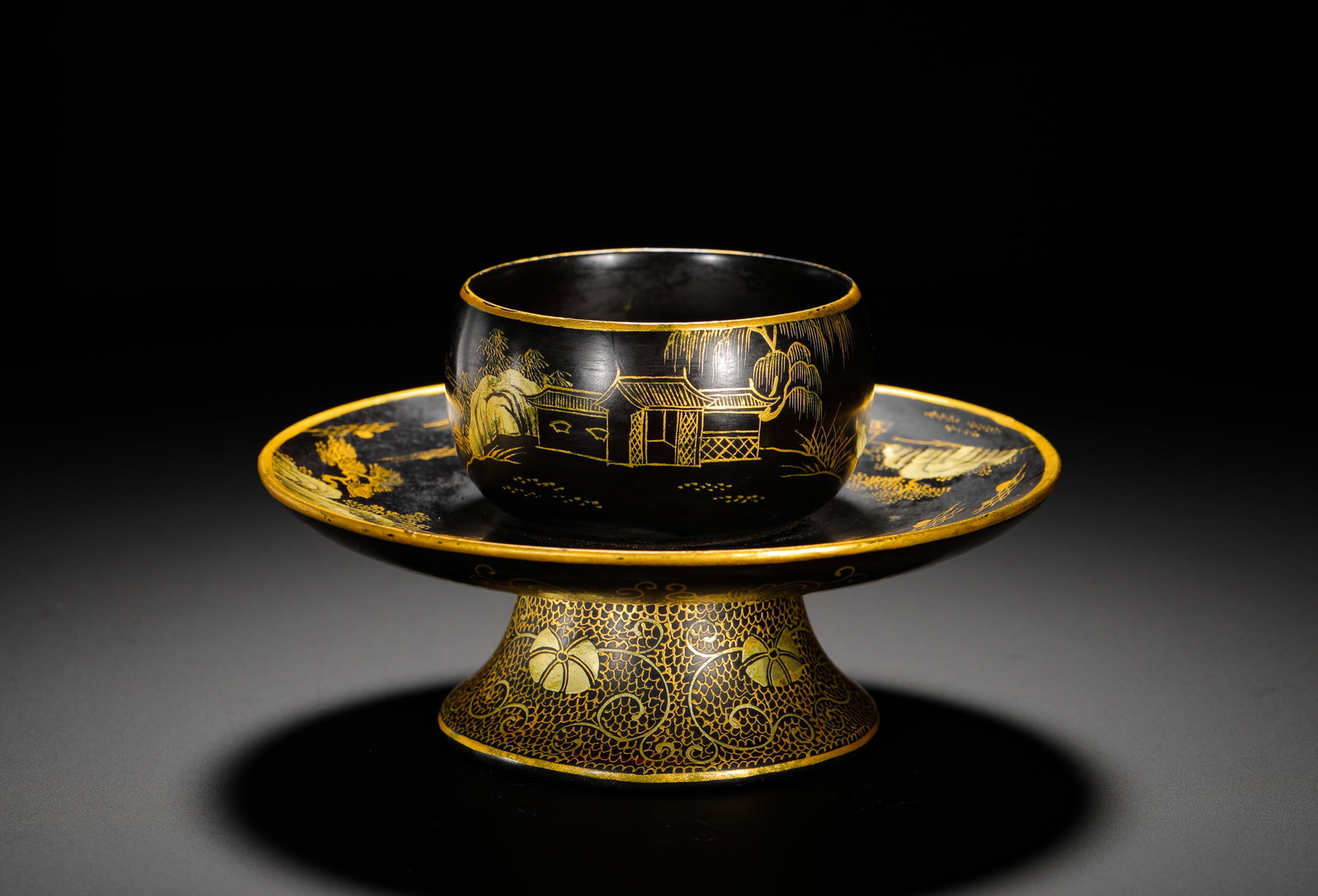 A BLACK LACQUER HIGH-FOOTED CUP HOLDER FROM THE QIANLONG PERIOD OF THE QING DYNASTY: Height:9cm (3.54in) Width:16cm (6.30in) Weight:130g(0.29lb)Black lacquer gold-painted tea cup and stand set, landscape pavilion patterns, inscribed "Made in Qianlong reign of Qing Dynasty" on base, an