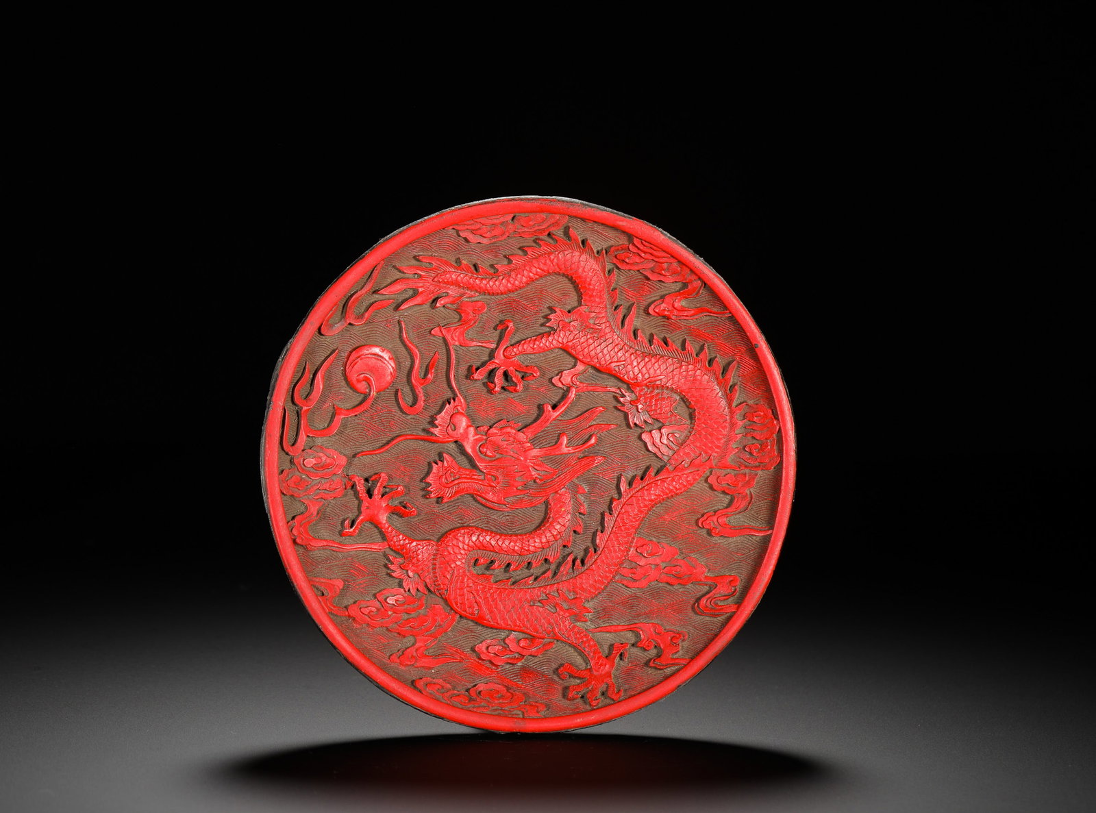 QING DYNASTY RED SEA WATER DRAGON PATTERN ROUND PLATE: D:14.5cm (5.71in) Weight:150g(0.33lb)Carved red lacquer round plate with dragon chasing pearl over wave patterns, black lacquer base inscribed "Collected by Xuhua Hall", antique carved lacquer ornamen