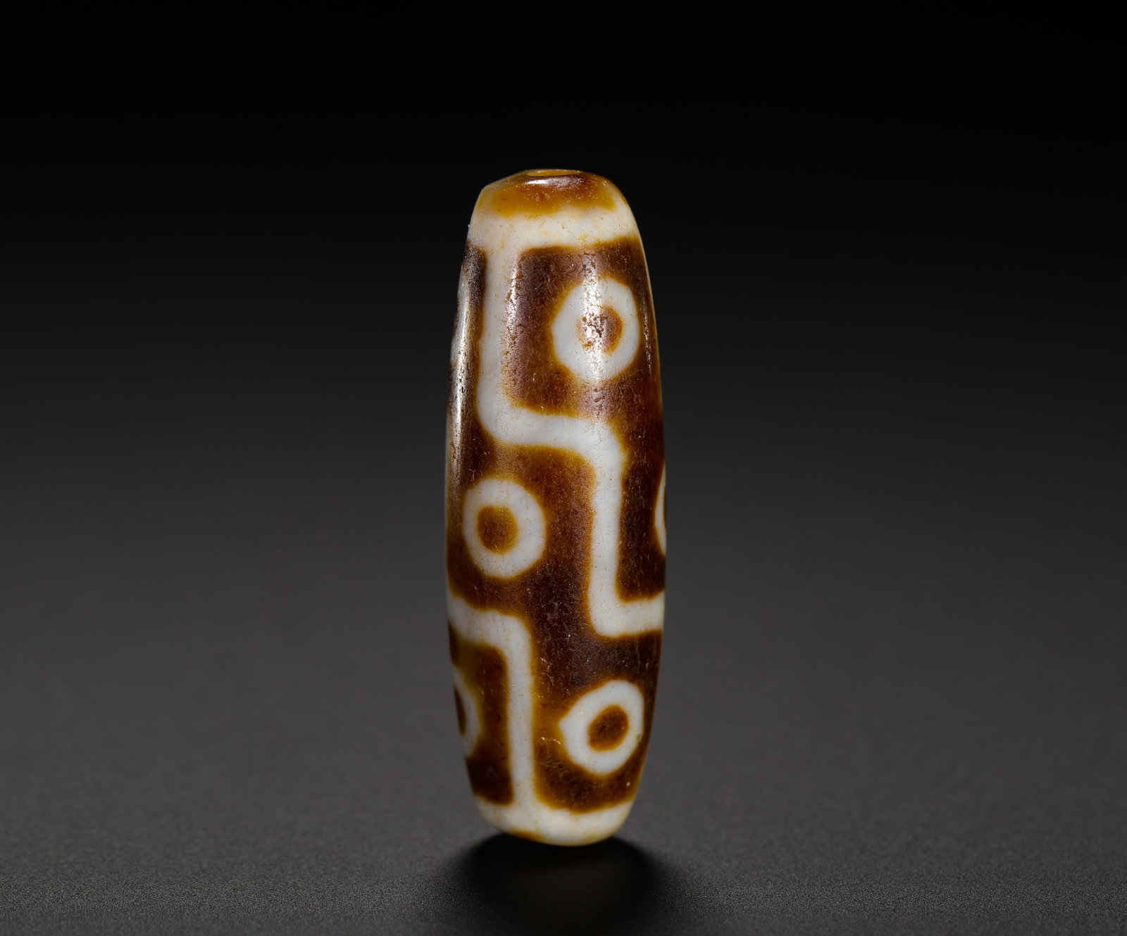 SIX-EYED ANCIENT SKY BEADS: Height:4cm (1.57in) Weight:10g(0.02lb)Six-eye ancient dzi bead made of elongated oval agate, etched with six circular eye totems connected by broken lines in cream white against dark brown base. The b