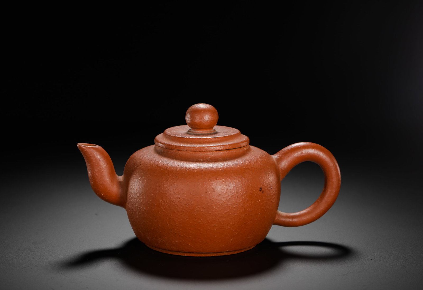 XU YOUQUAN ZHU CLAY PURPLE CLAY TEAPOT: H:10cm W:18cm Weight:410g Plain small Zisha teapot of natural coarse-grain vermilion clay with granular texture. Plump spherical body, short curved spout for smooth water flow, well-proportioned circu