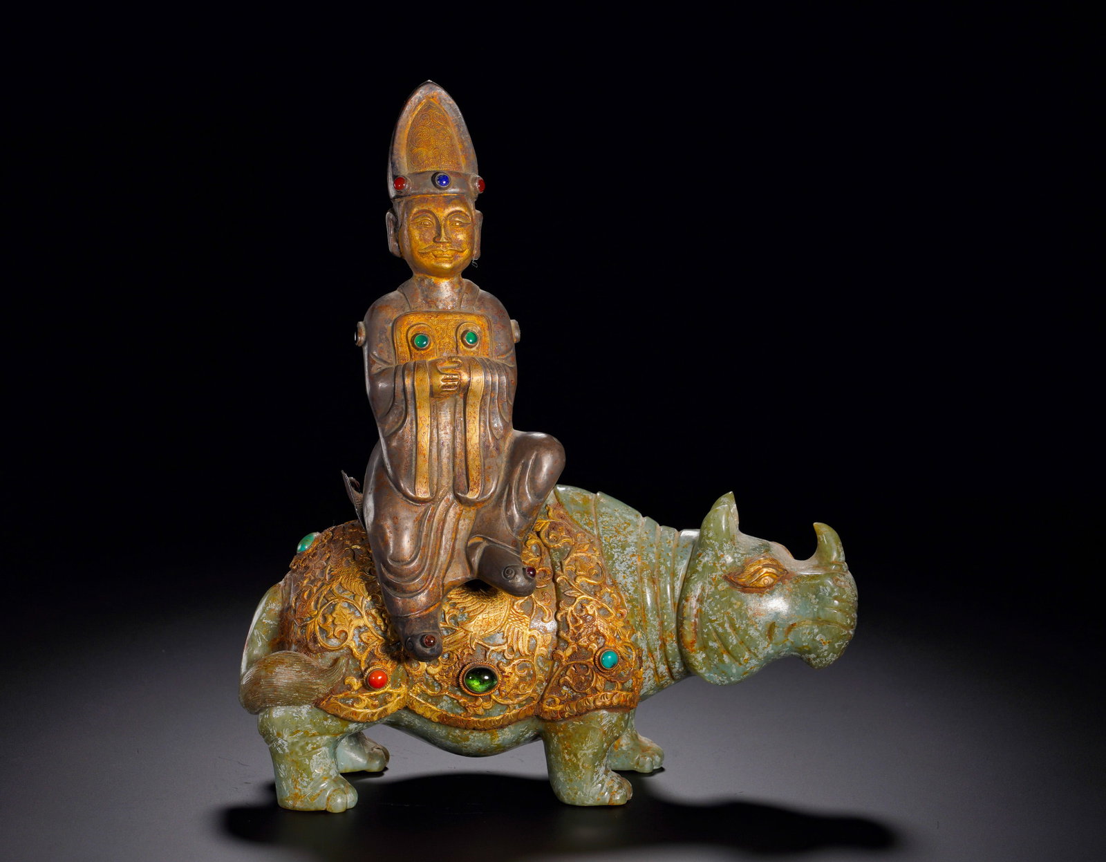 HAN DYNASTY GREEN JADE INLAID WITH GOLD AND TREASURE RIDING RHINOCEROS IMMORTAL: Height:23cm (9.06in) Width:21cm (8.27in) Weight:1870g(4.12lb)The green jade rhinoceros is surmounted by gilded bronze figure of immortal holding jade tablet. Saddle ornament inlaid with turquoise and 