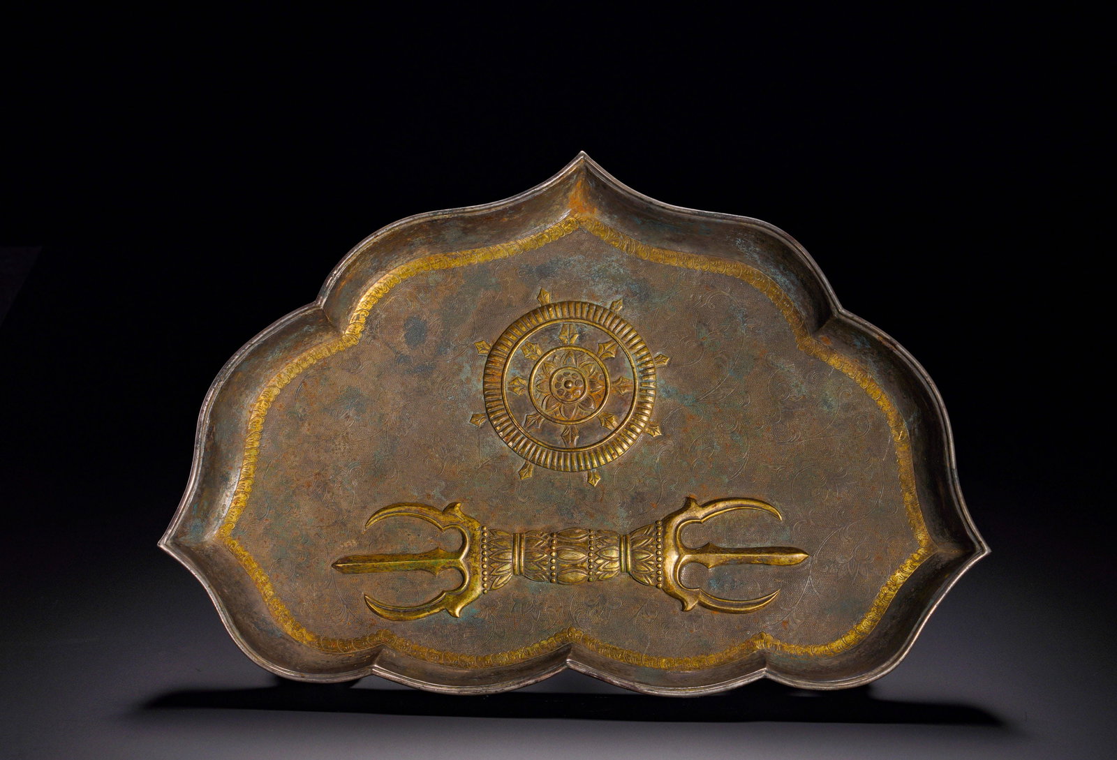 A TANG DYNASTY SILVER-GILDED TRIDENT DHARMA WHEEL PATTERN PLATE: Height:6.5cm (2.56in) Width:30cm (11.81in) Weight:530g(1.17lb)The silver plate with scalloped rim stands on three gilt beast-head feet. The interior embossed with gilded Buddhist trident and dharma wh
