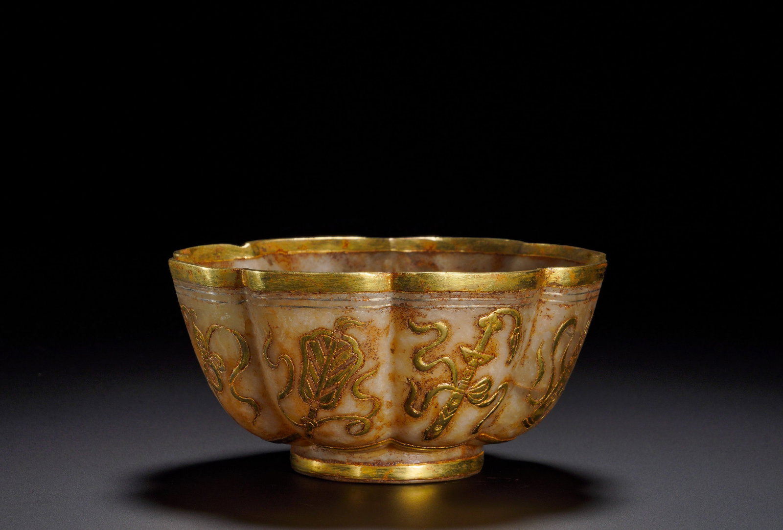 WHITE JADE INLAID WITH GOLD DARK EIGHT IMMORTALS FLOWER-MOUTHED BOWL OF THE TANG DYNASTY: Height:5.5cm (2.17in)Width:10.6cm (4.17in)Weight:190g(0.42lb)Tang Dynasty white jade lobed bowl with gilded Eight Immortals emblems.Petal-form jade vessel mounted with gilded rim and foot. Gilded inla
