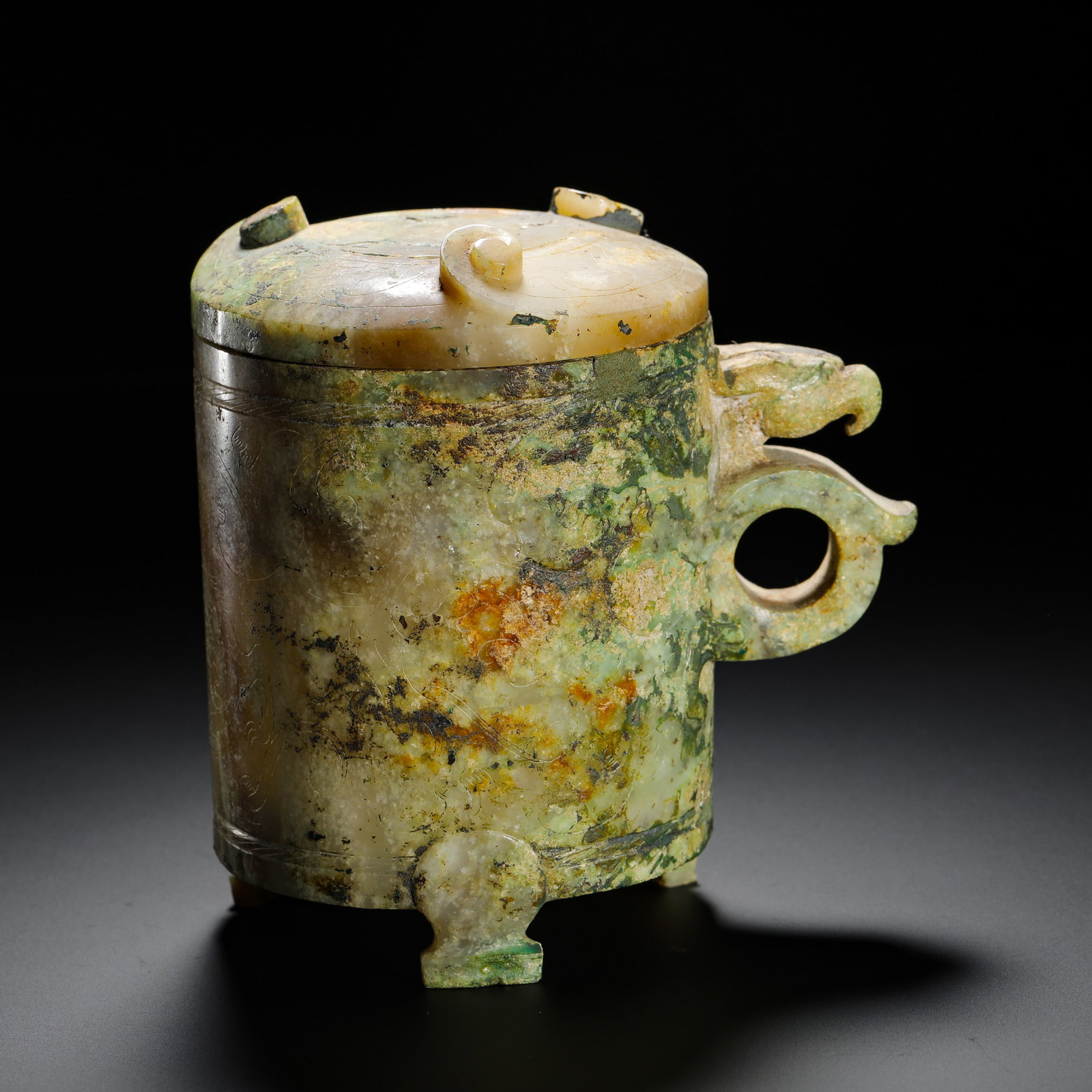 HAN DYNASTY HETIAN JADE PHOENIX HEAD HANDLE THREE-LEGGED COVER ?: H:13cm W:11.5cm Weight:570g Han Dynasty jade wine vessel carved with phoenix-shaped ring handle, covered in aged red-green patina, with three feet and lidded top, a ritual utensil for noble feasts