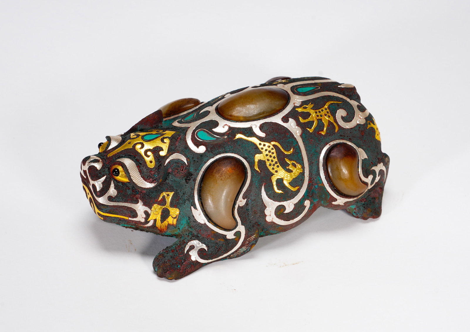 BRONZE FROM THE WARRING STATES PERIOD WITH INLAID GOLD AND SILVER INLAID JADE AUSPICIOUS BEAST: Height:5.5cm (2.17in) Width:12.5cm (4.92in) Weight:530g(1.17lb)Recumbent bronze relic decorated with interwoven beast scrolls in gold and silver wire, embedded oval jade cabochons and turquoise. Zoomo