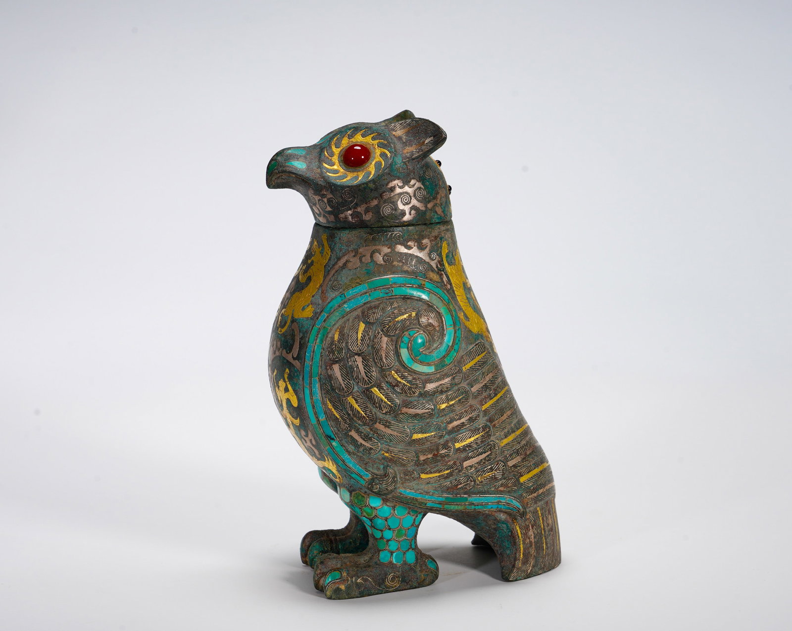 BRONZE WITH INLAID GOLD AND SILVER AND TURQUOISE OWL COVER FROM THE WARRING STATES PERIOD: Height:19cm (7.48in) Width:13.5cm (5.31in) Weight:1270g(2.80lb)Integrated bronze vessel modeled as sacred standing owl, removable lid, inlaid gemstone eyes, feather patterns in gold and silver wire, t