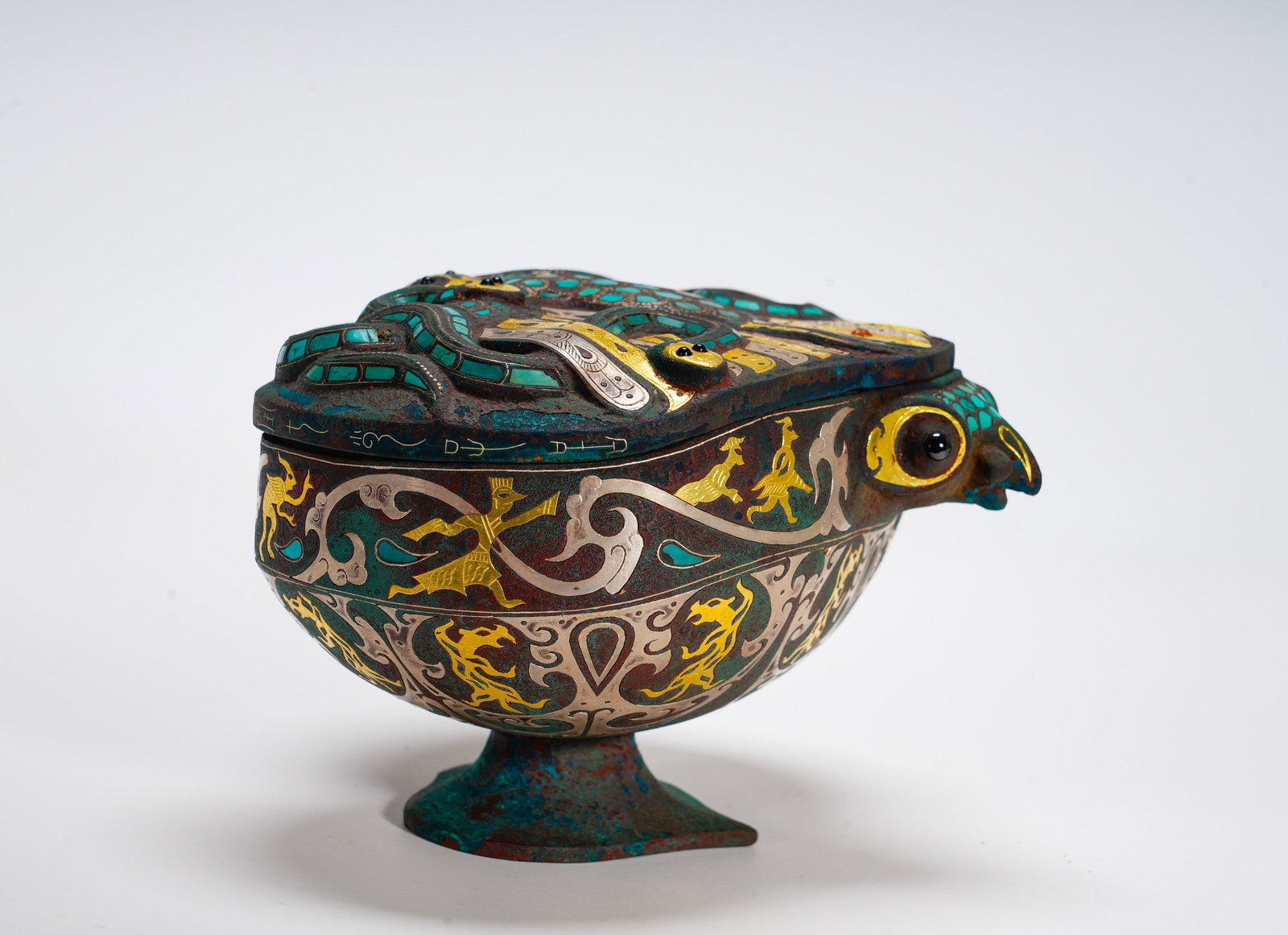 BRONZE INLAID WITH GOLD AND SILVER INLAID WITH TURQUOISE DIVINE BIRD COVER BEAN FROM THE WARRING: Height:13cm (5.12in) Width:20cm (7.87in) Weight:620g(1.37lb)Stemmed bronze container fitted with sacred bird head, lid decorated with turquoise serpent pattern. Body carved with dancing figures and be