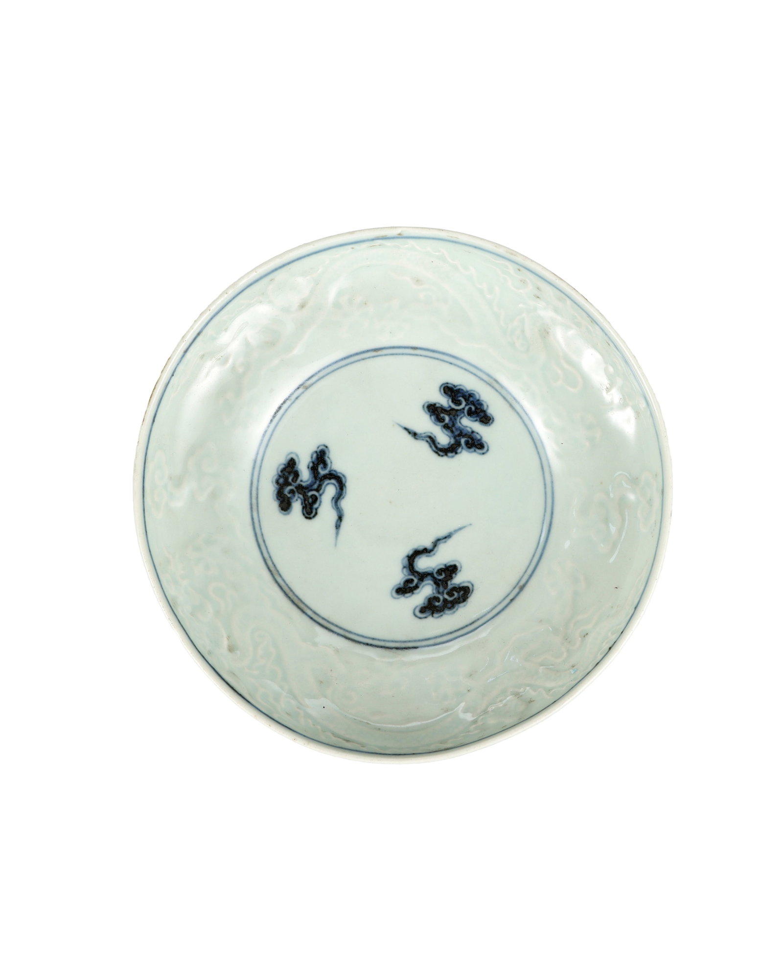 A BLUE AND WHITE PORCELAIN BOWL WITH DARK ENGRAVED CLOUD AND DRAGON PATTERNS: H:3.5cm W:16.7cm Interior close-up of a porcelain bowl. Three blue ruyi cloud patterns are enclosed within double blue circles at the center. The whole inner wall is finely incised with relief dragon 