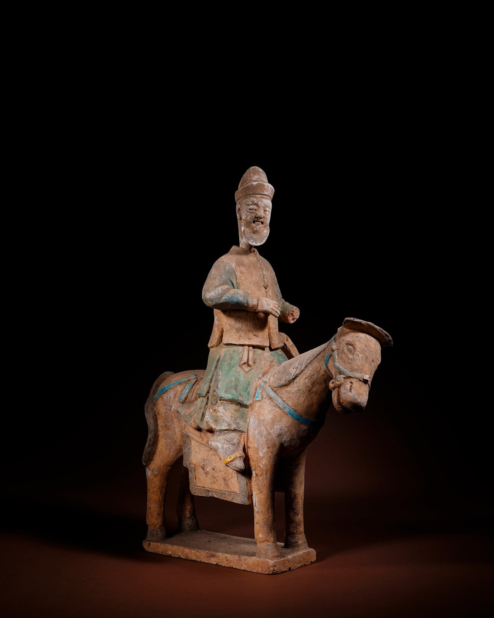 PAINTED MING DYNASTY TERRACOTTA FIGURES WITH LONG BEARDS ON HORSEBACK: L:27cm H:38.5cm This mineral-painted equestrian pottery figurine of Ming Dynasty is molded as an integrated piece of white clay, including figure, horse and square base, decorated with blue, green and