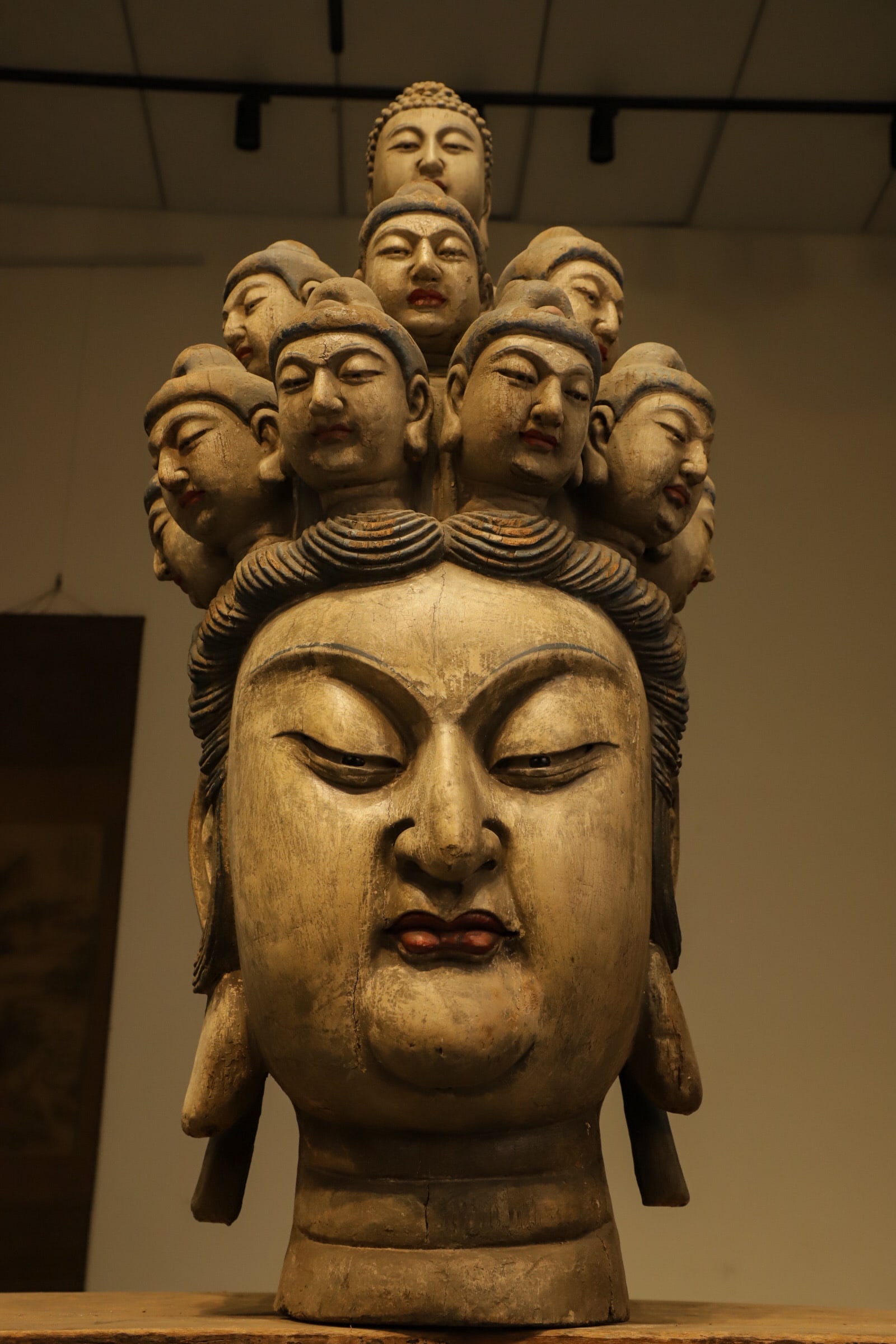 A WOODCARVING OF THE ELEVEN-FACED GUANYIN BODHISATTVA'S HEAD FROM THE MING DYNASTY: H:110cm (43.31in) L:52cm (20.47in) W:45cm (17.72in)This is a fragmented head sculpture of Eleven-headed Avalokite?vara Bodhisattva. The main head is large and plump, with gentle round facial features,