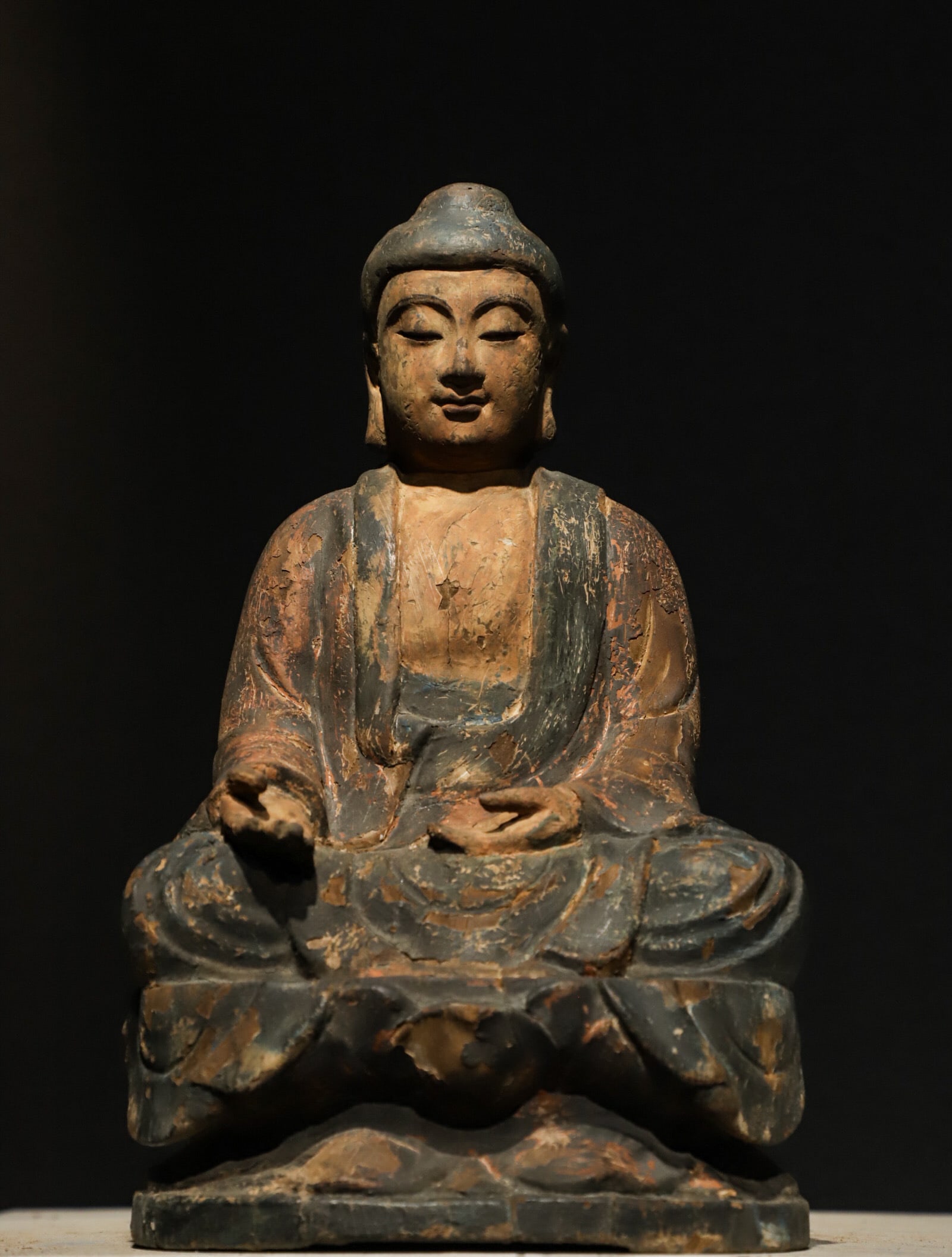 A WOODEN STATUE OF SAKYAMUNI BUDDHA FROM THE MING DYNASTY: H:28cm (11.02in)L:17.5cm (6.89in)W:15cm (5.91in)The solid heavy wood body bears naturally weathered cracked polychrome paint layers with faded aged traces, exposing mild vicissitudinous wood texture u