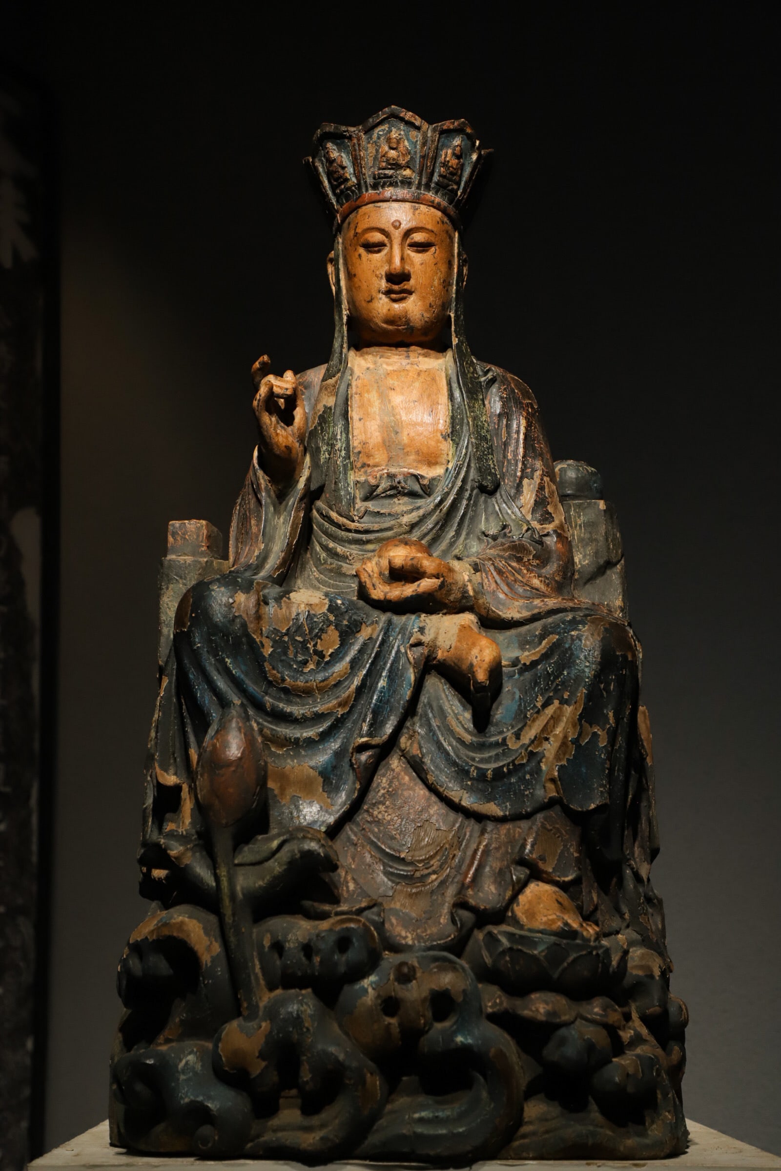A SEATED STATUE OF THE BODHISATTVA DIZANG IN PAINTED WOODCARVING FROM THE MING DYNASTY: H:65cm (25.59in) L:33cm (12.99in) W:28cm (11.02in)The statue is carved from a single block of wood and decorated with mineral-based paints in blue, vermilion and golden hues. Its aged lacquer coating 