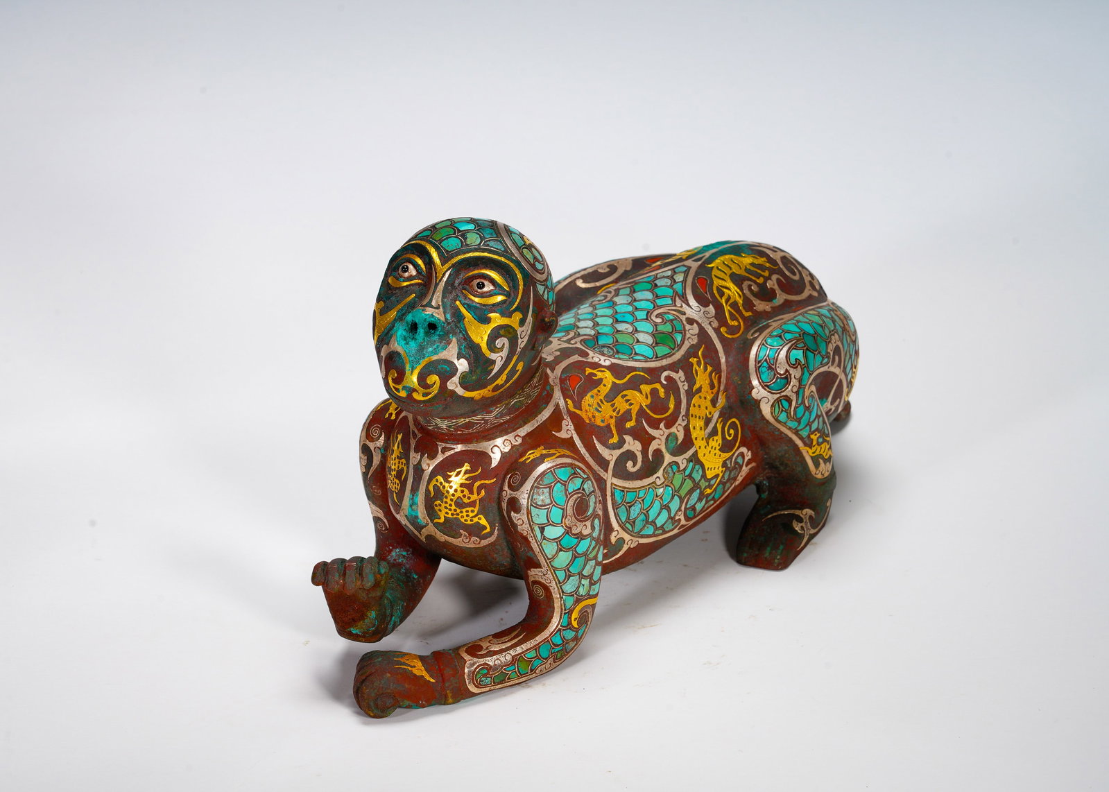 BRONZE INLAID WITH GOLD AND SILVER INLAID WITH TURQUOISE MONKEY FROM THE WARRING STATES PERIOD: Height:18cm (7.09in) Width:31cm (12.20in) Weight:2630g(5.80lb)Recumbent bronze monkey sculpture. Surface decorated with interlaced dragon scrolls in golden wire, turquoise mosaic on face and body. Mon