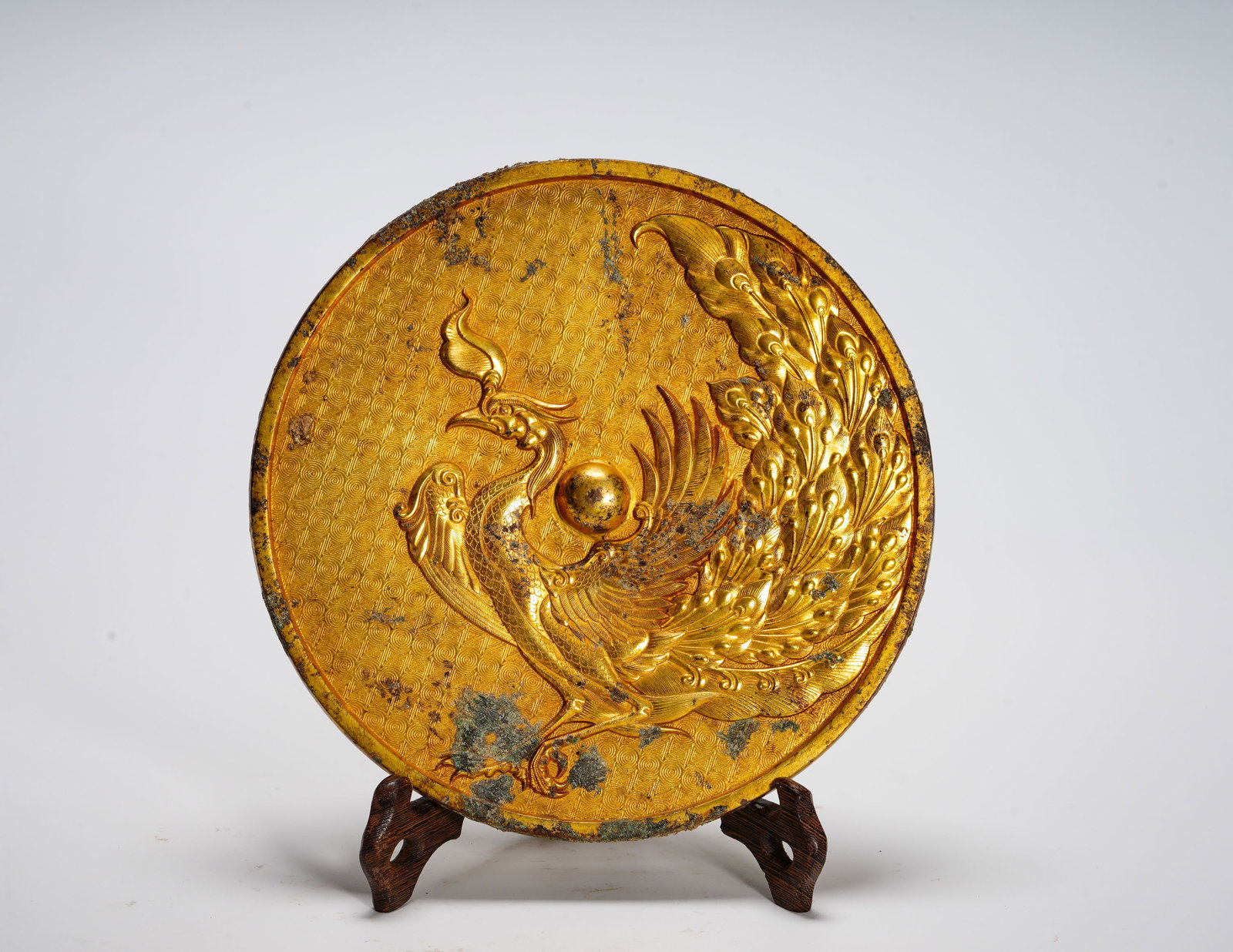 TANG DYNASTY GILDED BRONZE PHOENIX AND BIRD MIRROR: Diameter:19.7cm (7.76in) Weight:1890g(4.17lb)Gilded bronze relic carved with standing phoenix holding orb, cloud pattern background. Phoenix symbolizes auspicious omen and peaceful reign. It served as