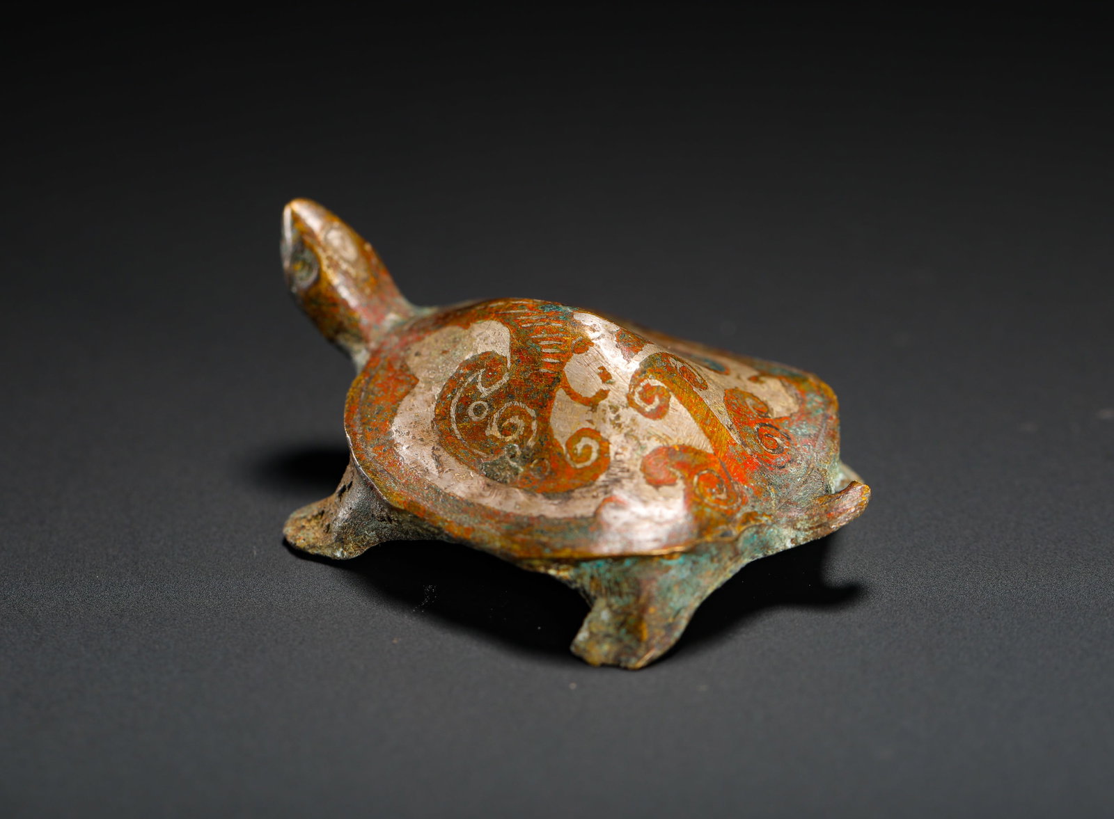 HAN DYNASTY INLAID SILVER PAINTED COPPER TURTLE TOWN: Height:2.3cm (0.91in) Width:5.2cm (2.05in) Weight:80g(0.18lb)Han Dynasty bronze turtle paper weight inlaid with silver scroll patterns and vermilion pigment. Solid bronze carving with natural green an