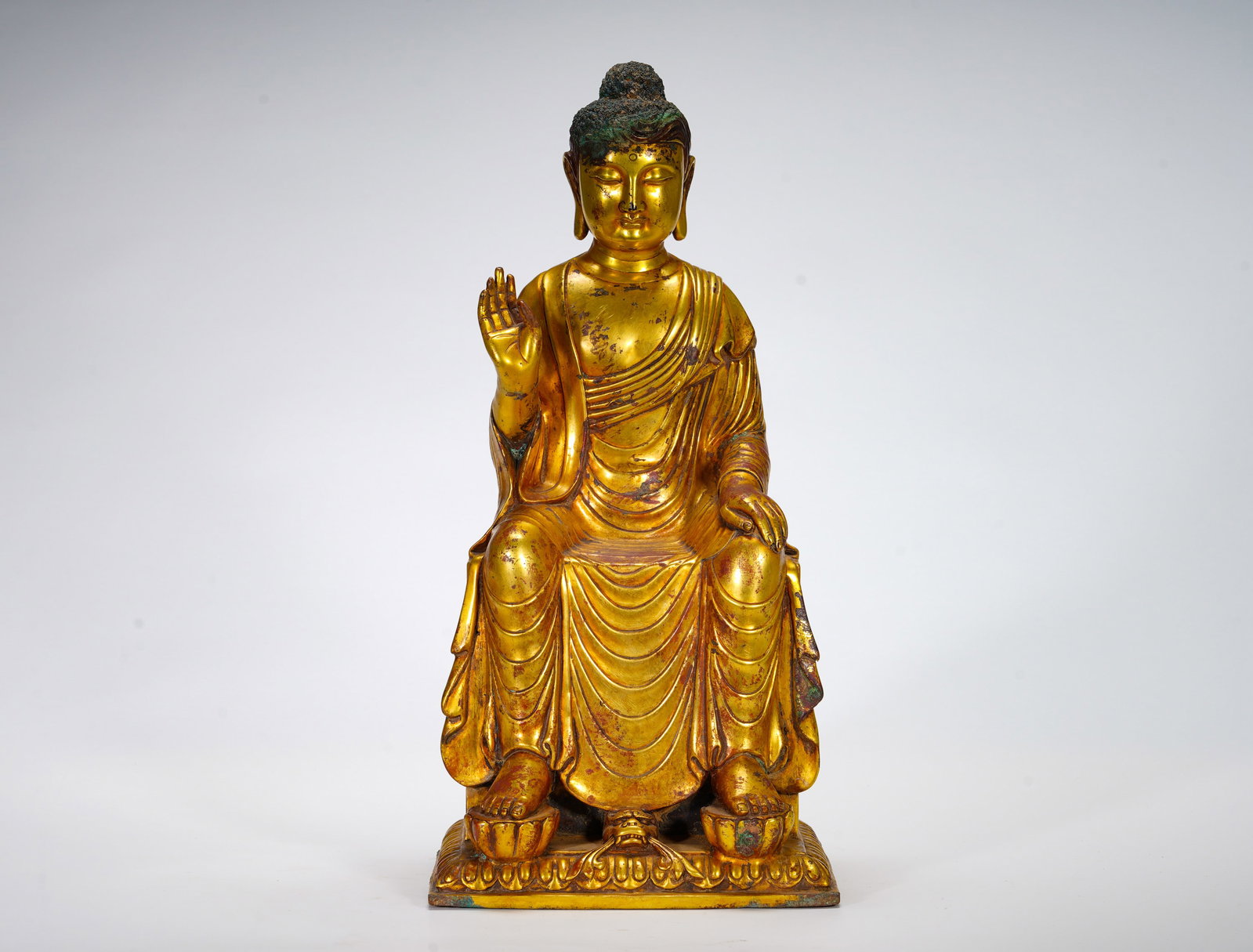 TANG DYNASTY GILDED SAKYAMUNI PREACHING SITTING BUDDHA: Height:39cm (15.35in) Width:19cm (7.48in) Weight:7600g(16.75lb)Bronze Buddha in relaxed sitting posture, right hand in abhaya mudra, symbolizing fearlessness and Dharma teaching. Wavy ushnisha, draped