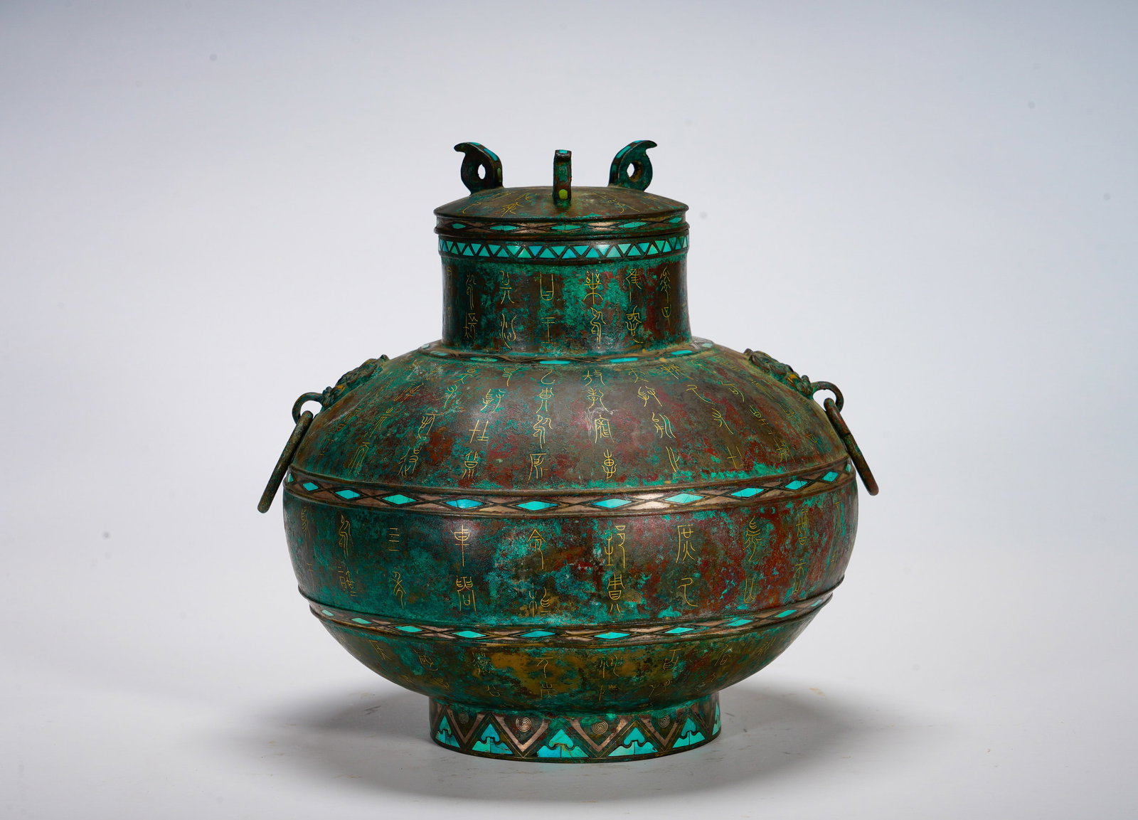 BRONZE POT WITH GOLD INSCRIPTIONS AND TURQUOISE INLAYS FROM THE WARRING STATES PERIOD: Height:23cm (9.06in) Width:25cm (9.84in) Weight:2940g(6.48lb)Bulbous bronze wine pot with lid, beast-ring handles. Inscribed golden characters, turquoise geometric border ornament. Hu used for ceremon