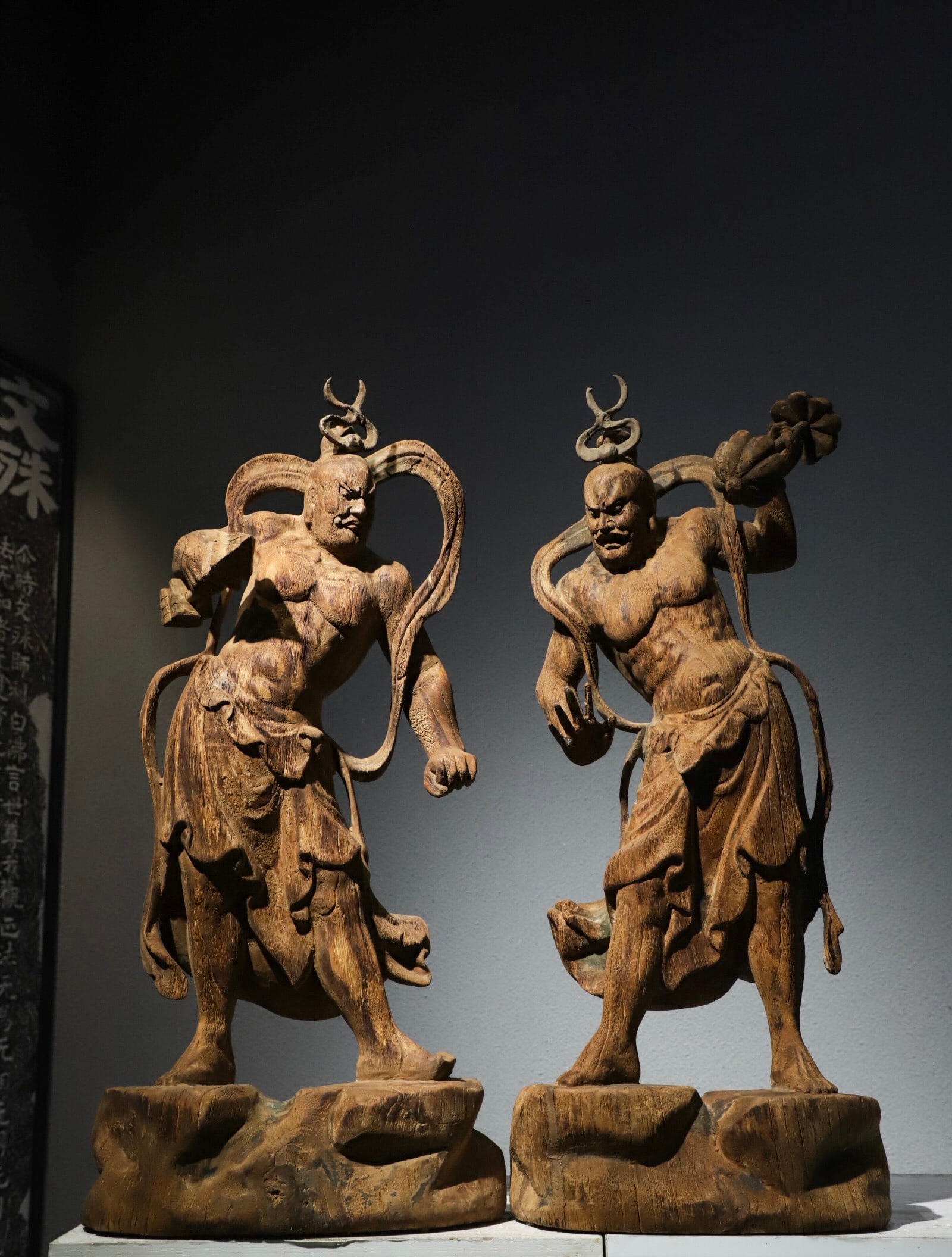 A STANDING STATUE OF THE TWO GENERALS, HENG AND HA, WHO WERE CARVED IN WOOD FROM THE SONG DYNASTY: H:70cm (27.56in) L:32cm (12.60in) W:16cm (6.30in)Two separately solid wood carved temple guardians without pigment finish; powerfully muscled bodies standing on irregular rocky plinths, originally ens