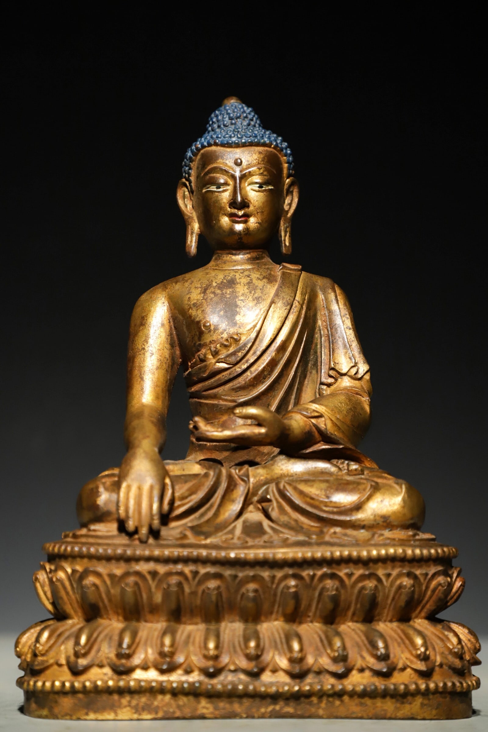 A GILDED BRONZE STATUE OF SAKYAMUNI BUDDHA FROM THE QING DYNASTY: Weight:2500g(5.51lb);H:22cm (8.66in) L:15cm (5.91in) W:10cm (3.94in)A gilded bronze Buddha Shakyamuni statue depicting the Enlightenment, seated in full lotus posture on double-layered lotus base, wit