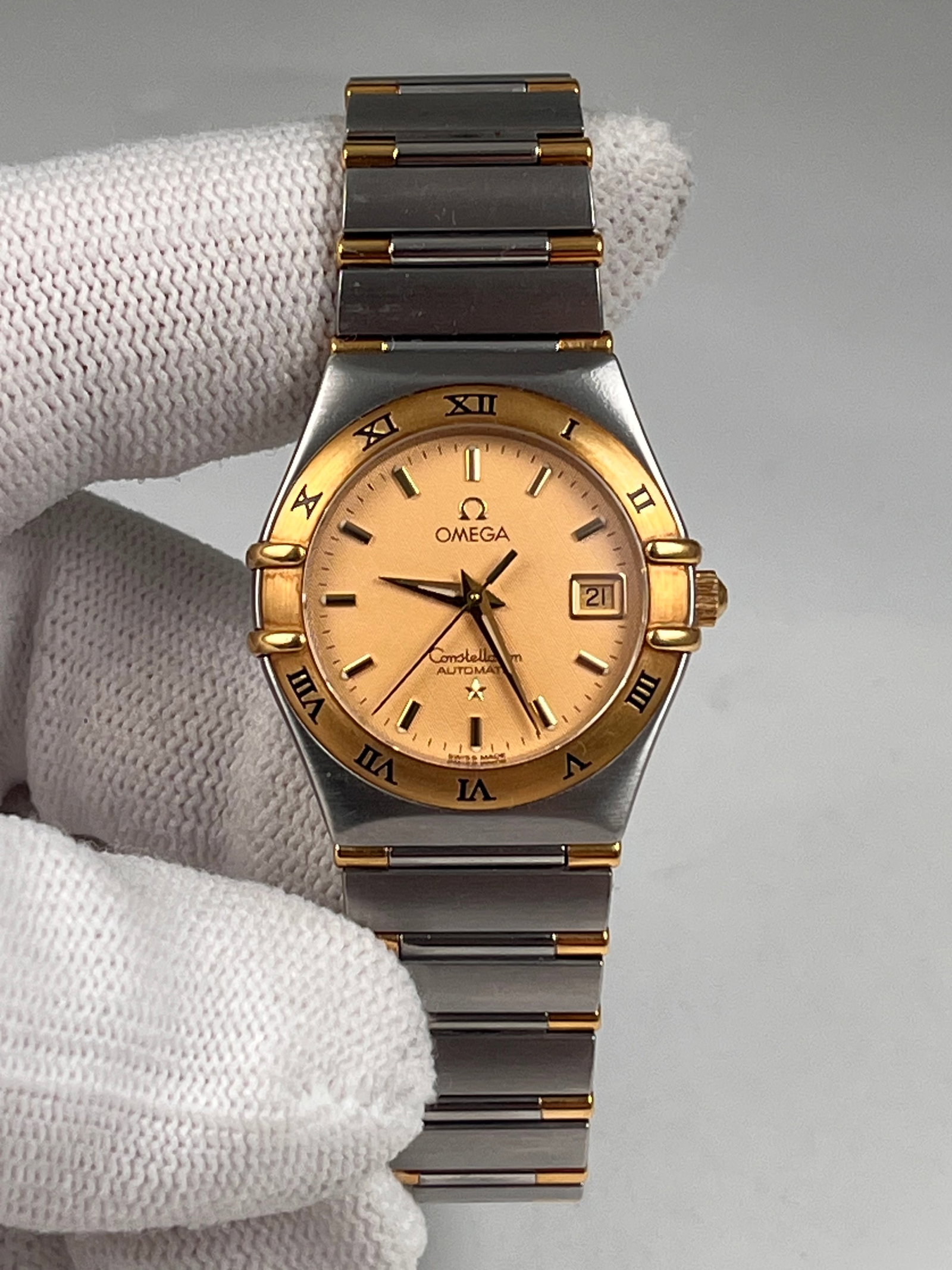 OMEGA CONSTELLATION WATCHES: A 27mm gold-tone case with a golden brushed dial, automatic mechanical movement, date display, and classic Roman numeral bezel with claw design