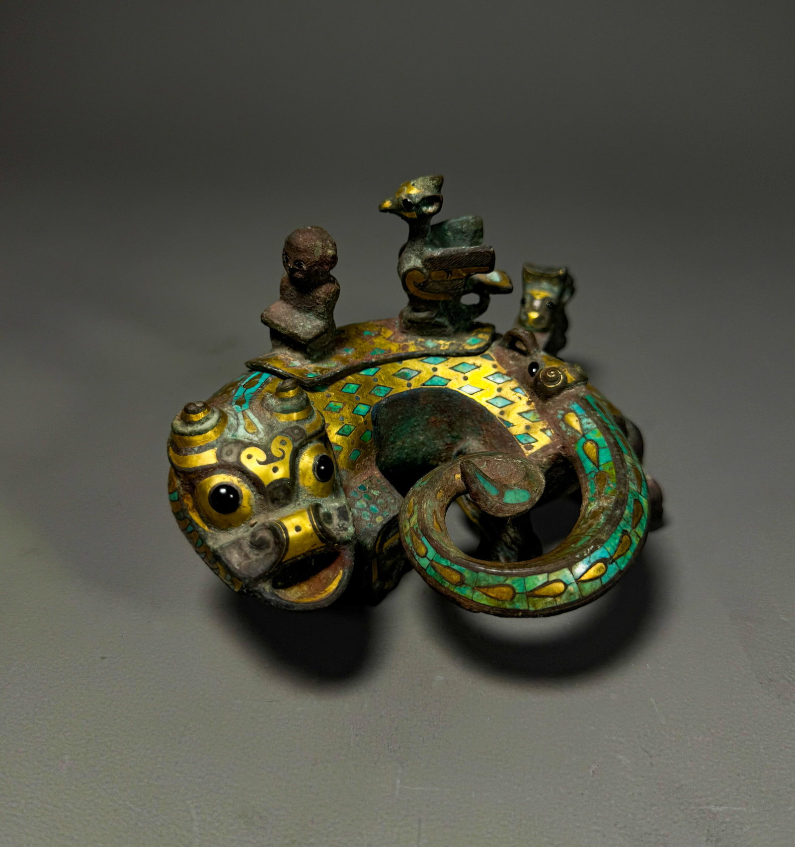 BRONZE FROM THE WARRING STATES PERIOD WITH GOLD INLAID TURQUOISE DIVINE FIGURES AND AUSPICIOUS: Height:8cmWidth: 11cmWeight:473gWarring States Period, Bronze Ornament with Figure and Mythical Beast, Inlaid Gold and Turquoise.This ritual ornament features a coiled mythical beast with gold