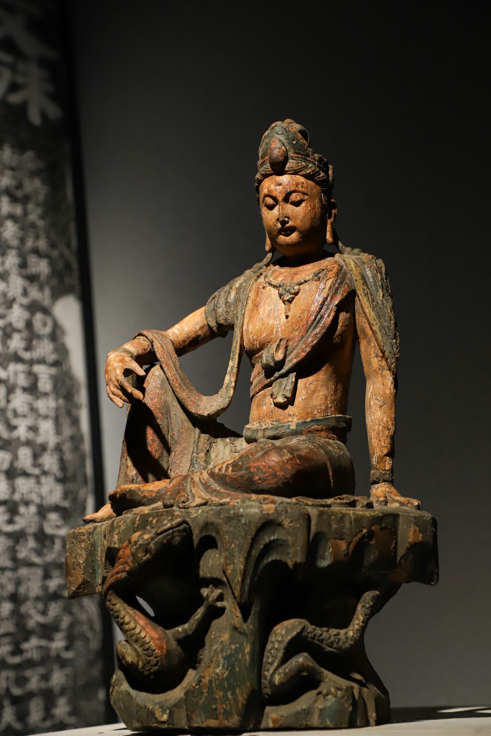A SITTING STATUE OF THE FREE-SPIRITED GUANYIN WITH PAINTED DRAGON PATTERNS ON A WOODEN BODY FROM THE: Height:46cm(18.11in) Width:28cm(11.02in)Antique wooden painted free Avalokiteshvara of Song-Yuan period, carved dragon reliefs under seat, worn mineral pigment layers, Buddhist statue for warding off 