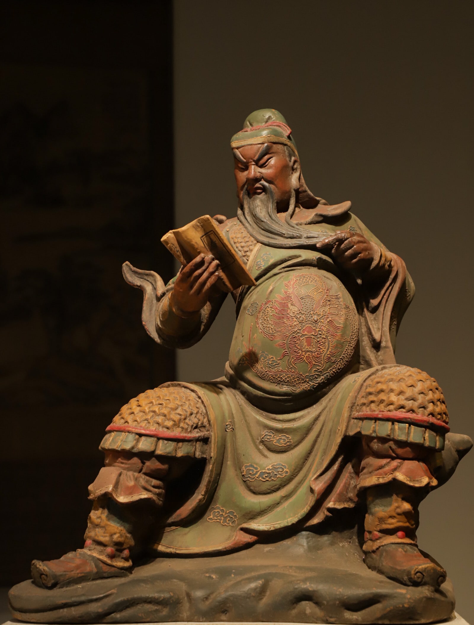 A SEATED STATUE OF GUAN GONG READING SPRING AND AUTUMN AT NIGHT, CARVED AND PAINTED IN WOOD FROM THE: Height:52cm(20.47in) Width:40cm(15.75in)Antique Qing wooden painted Guan Yu statue reading classics, worn mineral pigments, worshiped for loyalty, fortune and peace
