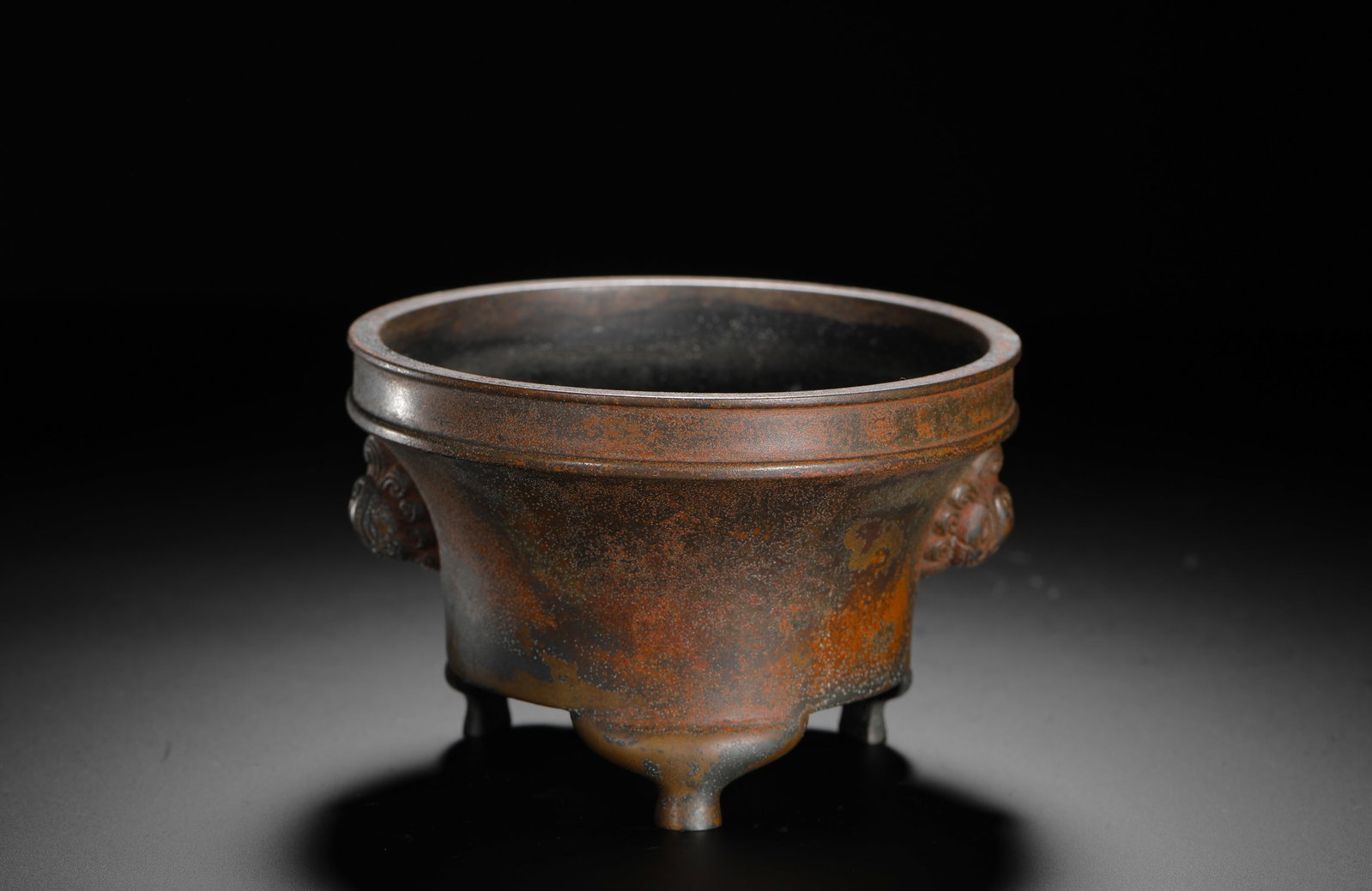 BRONZE LION-EAR THREE-LEGGED STOVE OF THE QING DYNASTY: H:8cm (3.15in) D:12cm (4.72in) Weight:900g (1.98lb)This is a Qing Dynasty bronze incense burner with a cylindrical body, lion-head handles on both sides, and three legs. The base is inscribed with "Xu