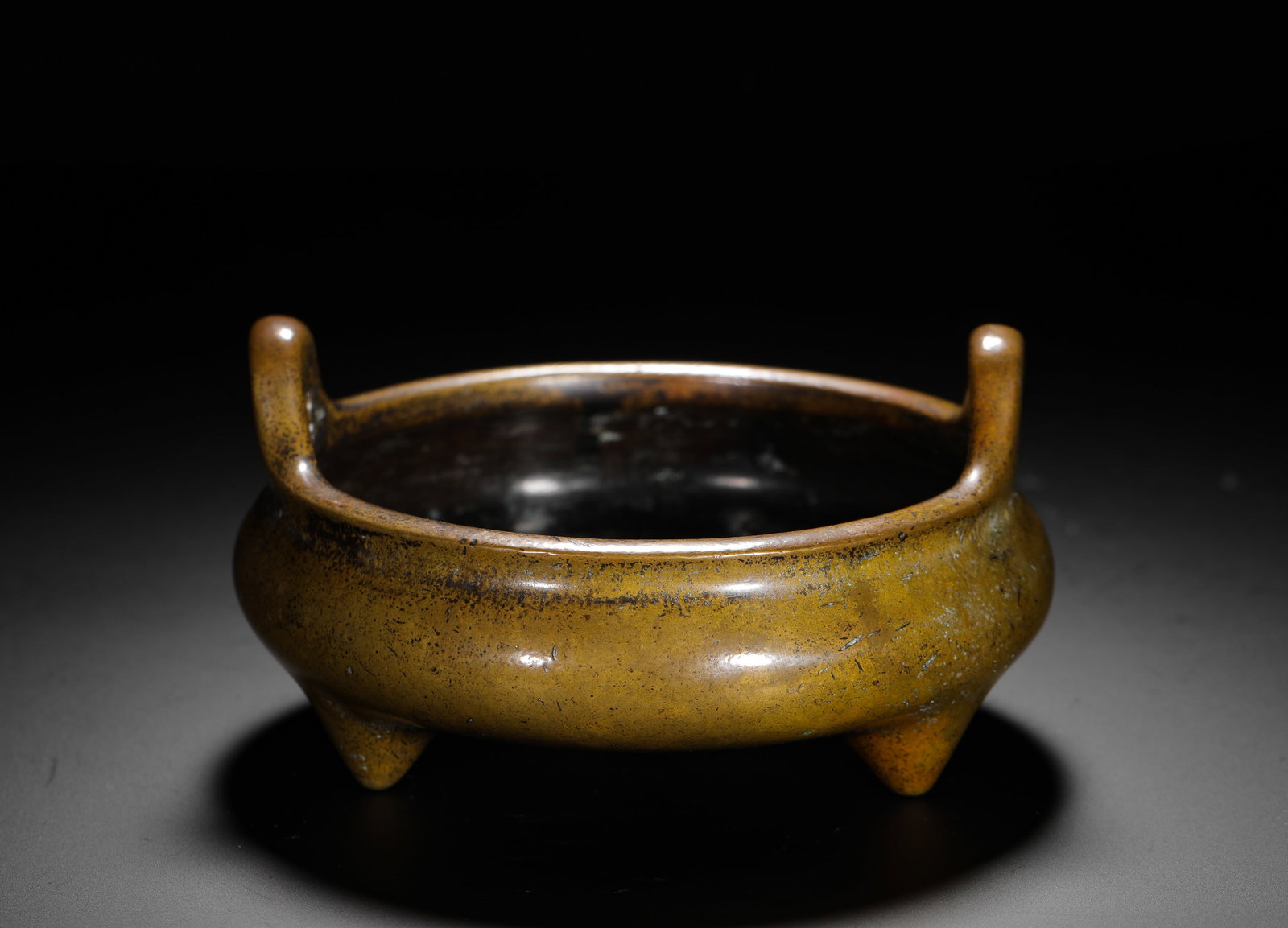 BRONZE THREE-LEGGED FURNACE WITH SKY-PIERCING EARS FROM THE QING DYNASTY: H:7cm (2.76in) W:13cm (5.12in) Weight:1000g (2.20lb) This is a Qing Dynasty bronze incense burner with a round body, upright ears on both sides, and three legs. The base is inscribed with "Xuande", ex