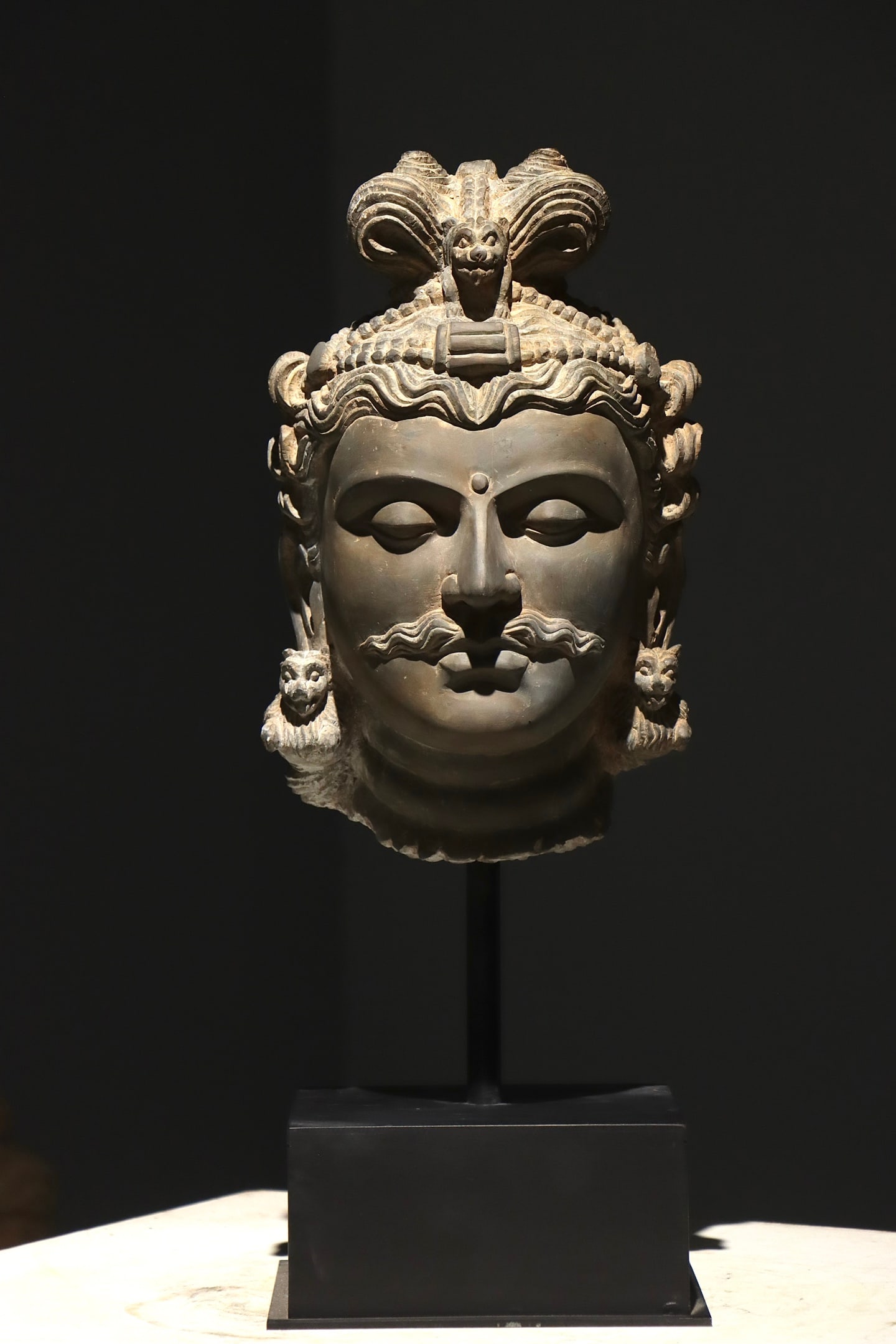 5 CENTURY GANDHARA GREY ROCK BODHISATTVA HEAD: Height:58cm(22.83in), Height:36cm(14.17in)Grey schist Bodhisattva head in classic Gandhara style. Wavy hair is finely carved; the crown is decorated with a beast motif at the centre. An urna sits on t