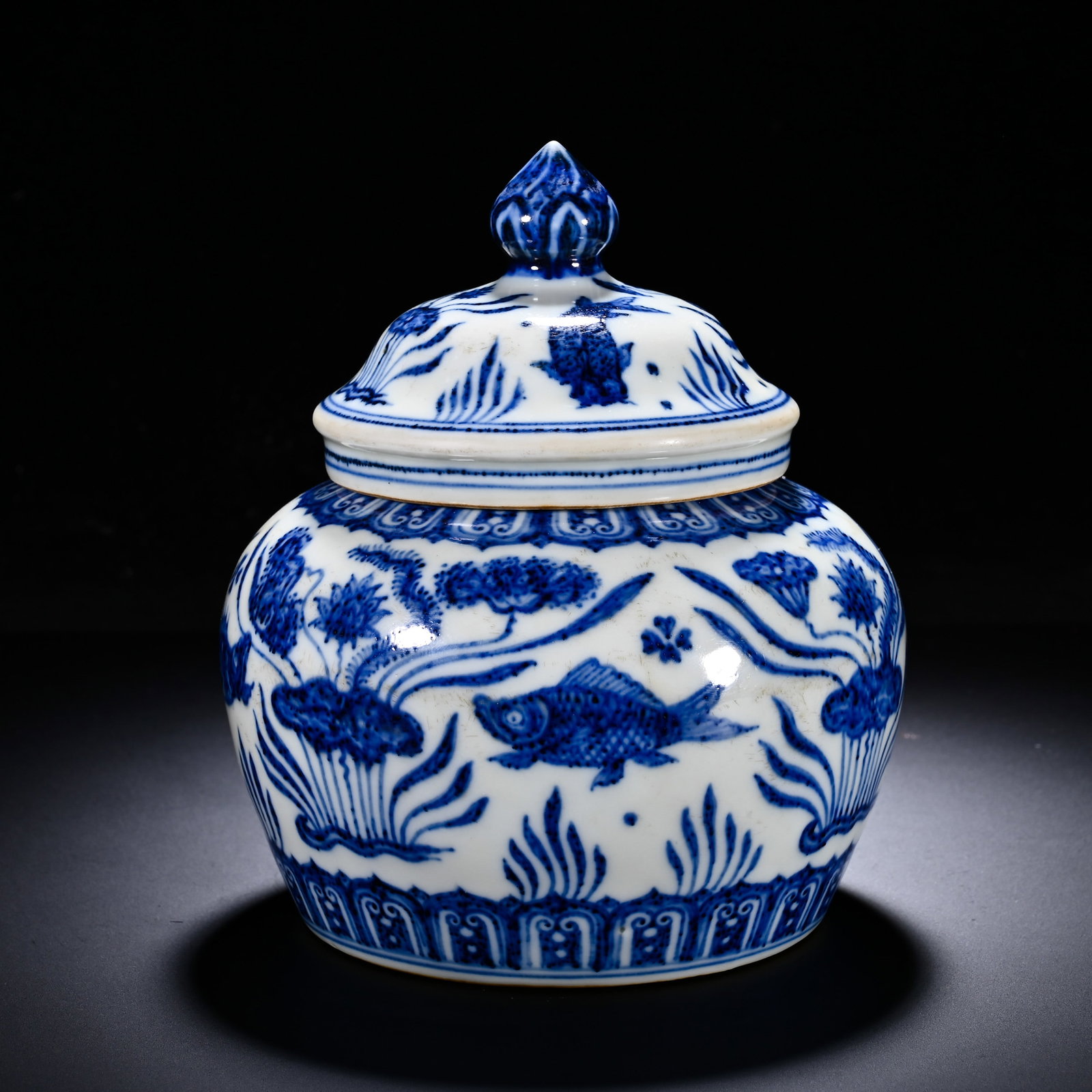MING XUANDE BLUE AND WHITE FISH AND ALGAE PATTERN COVERED JAR: Height:15cm (5.91in) , Diameter:13cm (5.12in) Covered jar with straight mouth, full shoulders, bulbous body and foot?ring, topped with pearl?form knob lid. Main body painted in under?glaze?blue with l