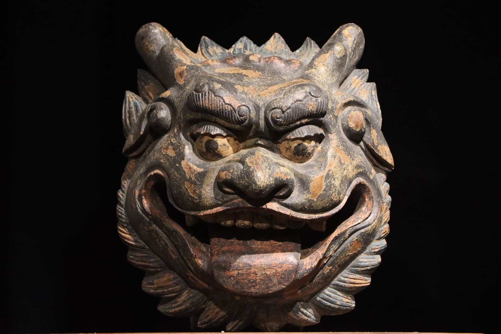 WOODBLOCK PAINTED BEAST HEAD MASK OF THE MING DYNASTY: H:40cm (15.75in) W:37cm (14.57in) Solid wood carved mythical beast mask with upright horns, curled eyebrow lines, wide staring eyes, broad open mouth with exposed teeth and tongue, and layered mane