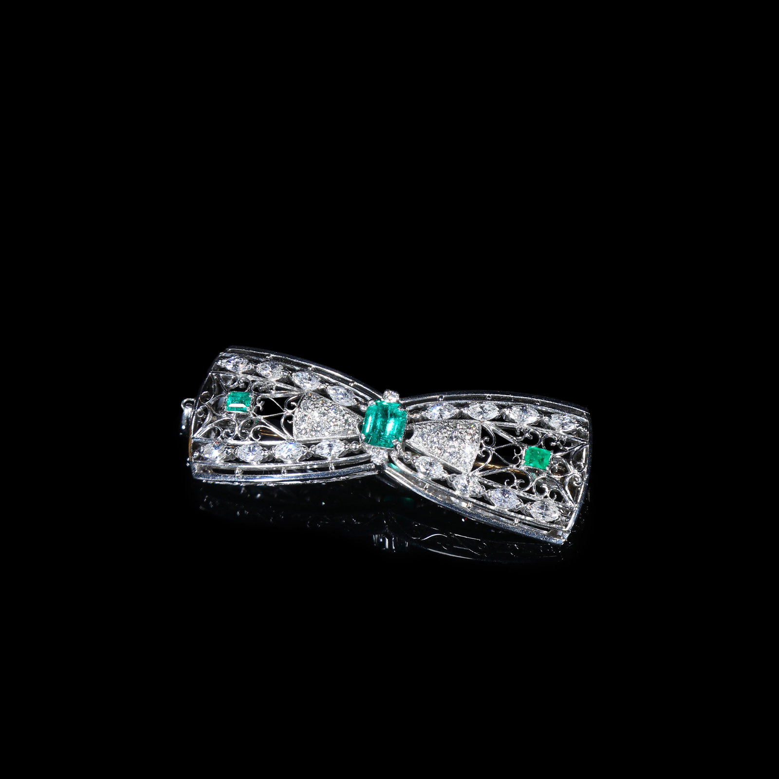 Edwardian-Period Platinum Emerald and Diamond Bow Brooch: 5.1*1.8cm Wt:15.82g Edwardian-period antique bow brooch crafted in platinum. Executed in the era-defining open-work lace filigree technique with delicate fine metalwork. Total emerald weight 1.5 carat