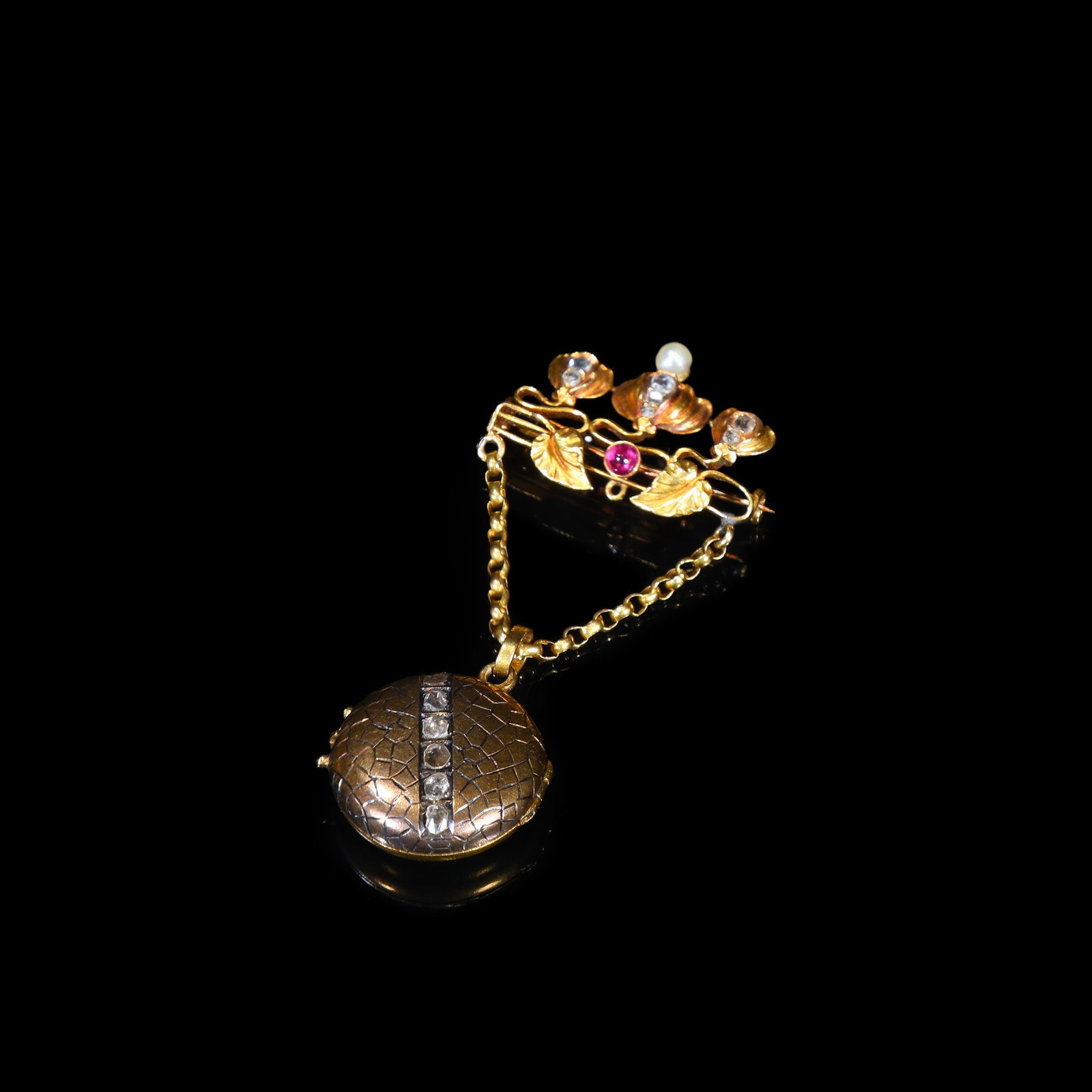 Victorian-Era (Circa 1870-1890) 18-Karat-Gold Ruby-and-Diamond Locket Pendant Brooch: 6*2.75cm Wt:8.08g Victorian-era (circa 1870-1890) 18-karat gold brooch. The foliate-styled brooch mount set with ruby. A chain suspends an opening locket engraved and vertically adorned with old-cut d