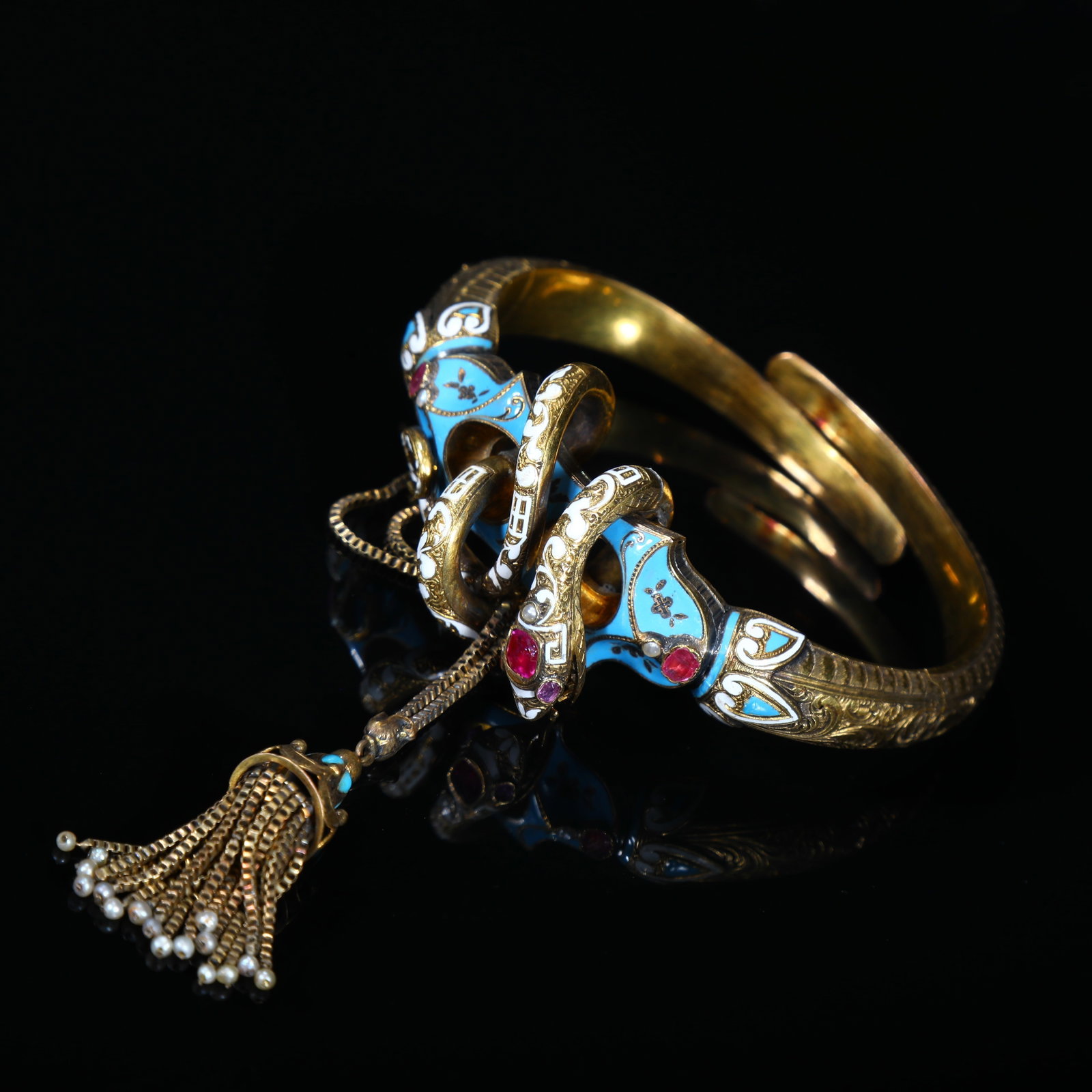 Victorian 19th-Century 18K-Gold Enamel Ruby Serpent Hinged Bangle with Tassel Pendant: Inner oval 6.3*4.93cm Wt:42.32g Victorian hinged serpent bangle, 19th-century, crafted in 18-carat-gold, decorated with vivid blue-and-white fired enamel, accented with ruby gemstones. Modelled as coi