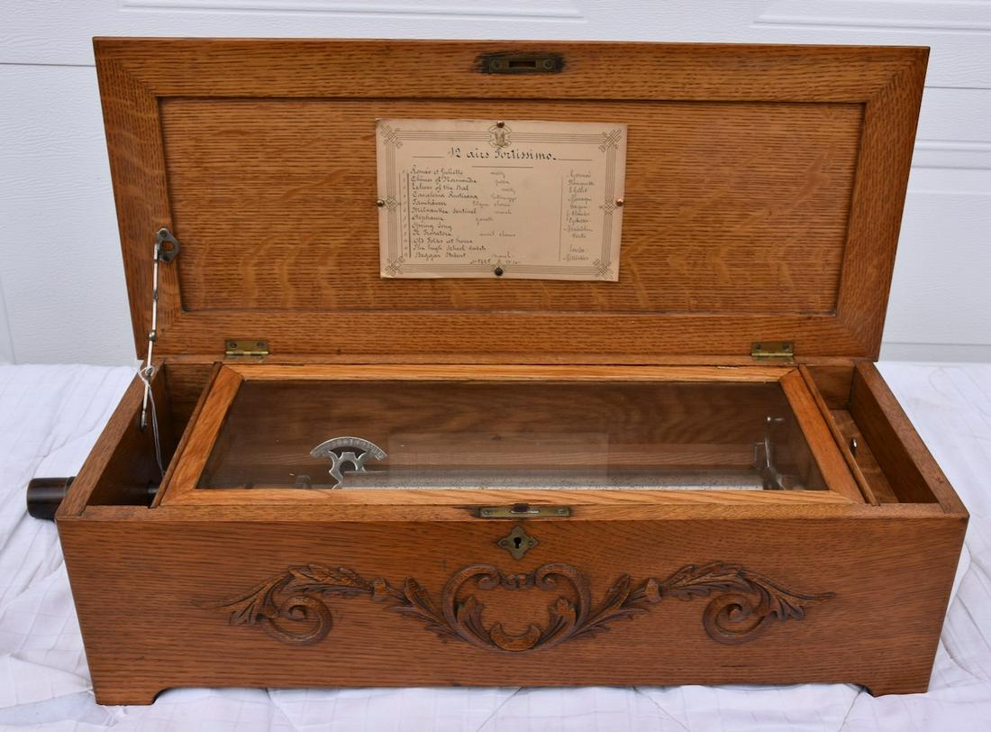 12 Tune Cylinder Music Box: Fortissimo. Has tune card and tune indicator. 13-1/2" cylinder. No broken teeth. Oak case with applied carving, outside crank style but no crank and double spring