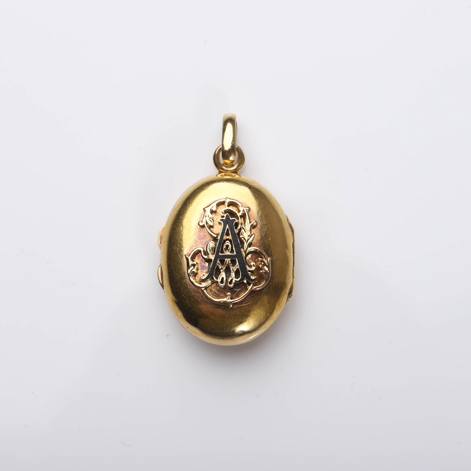 A VICTORIAN GOLD AND ENAMEL LOCKET PENDANT: Dimensions 1 1/4 × 13/16 in (31.6 × 21.4 mm); Weight: 8 g. Description: A fine oval gold locket from the Victorian period, centered with an applied monogram "A" in black enamel over a foliate scroll